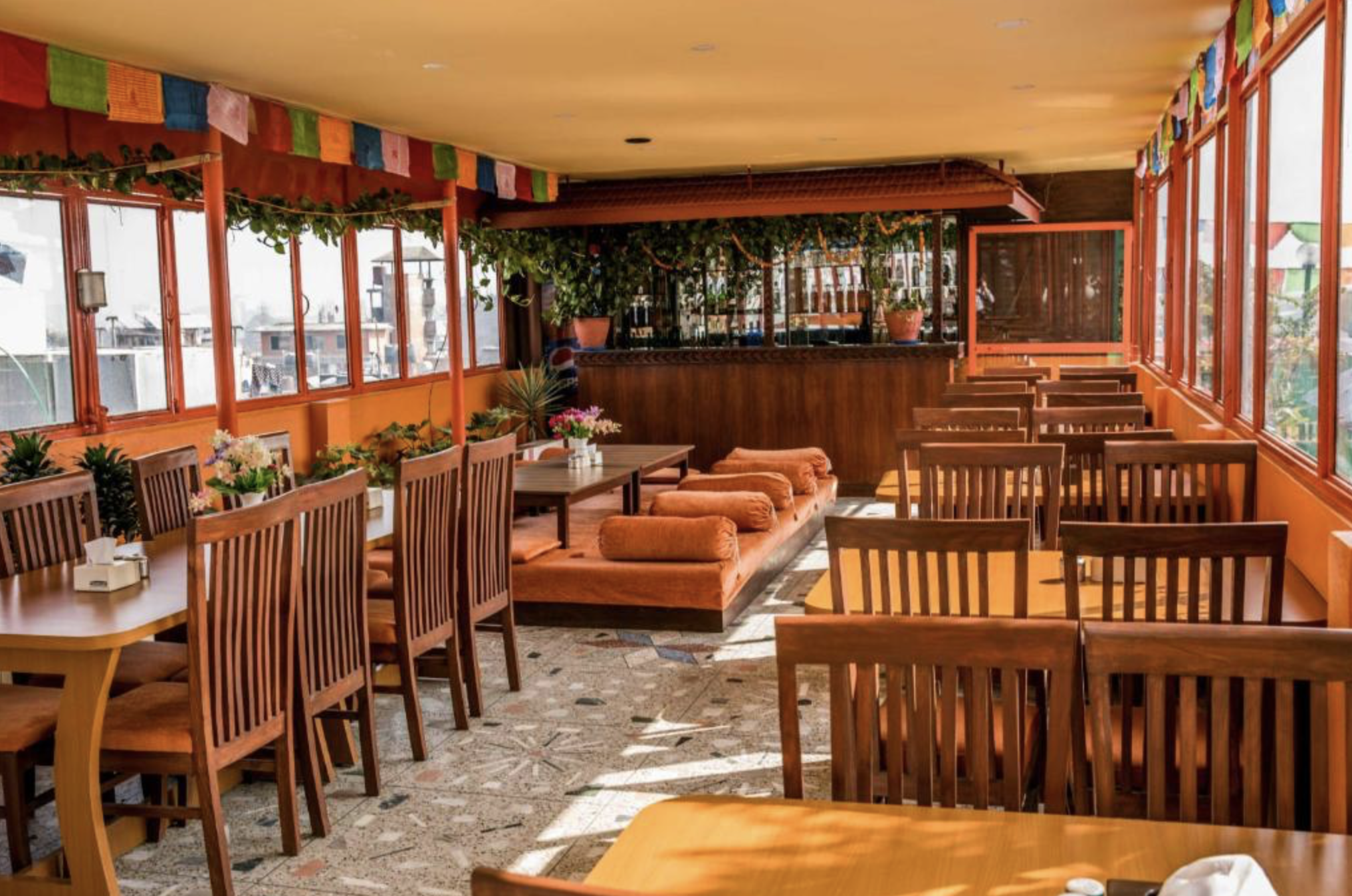 Sunny restaurant interior with wooden tables and chairs, colorful hanging flags, potted plants, and large windows letting in natural light. Wildlife expedition and phot safari with Wild Selection Tours.