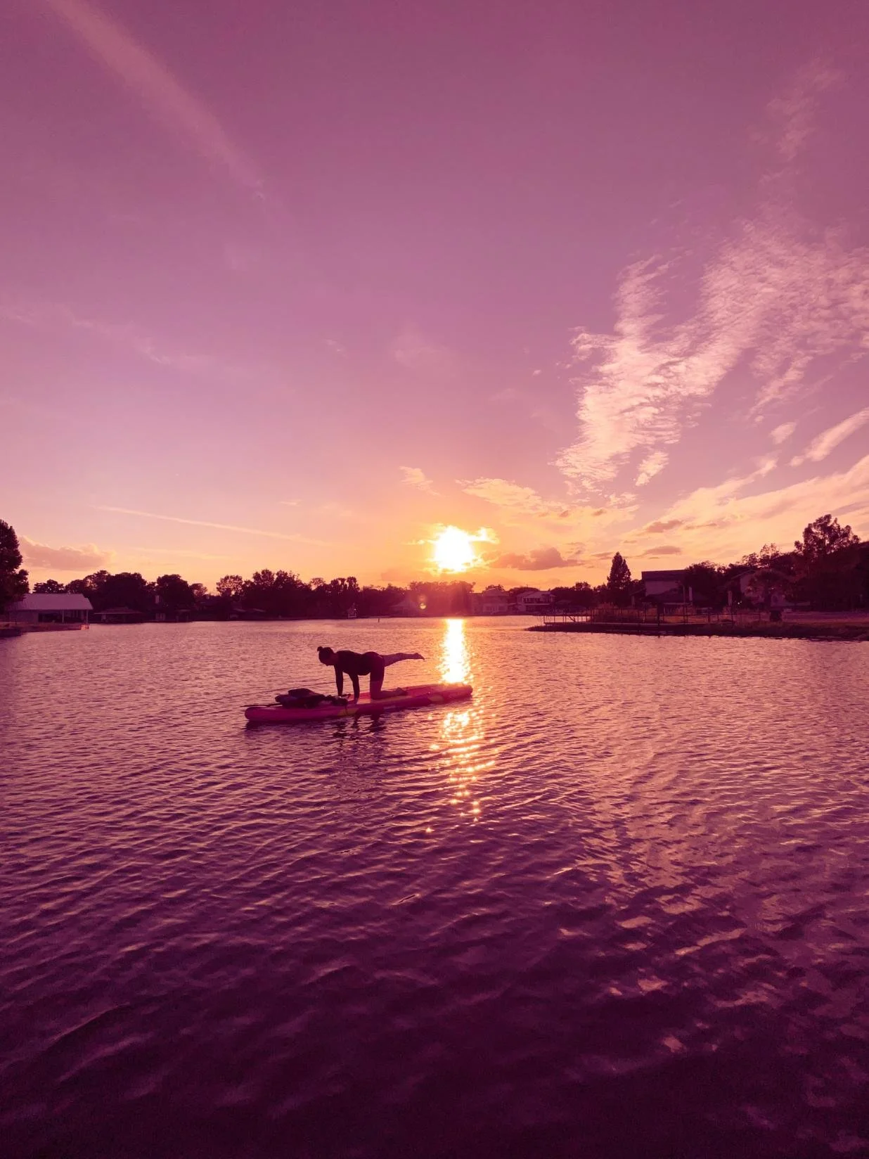 Person paddleboarding on a lake during a sunset with pink and purple sky.