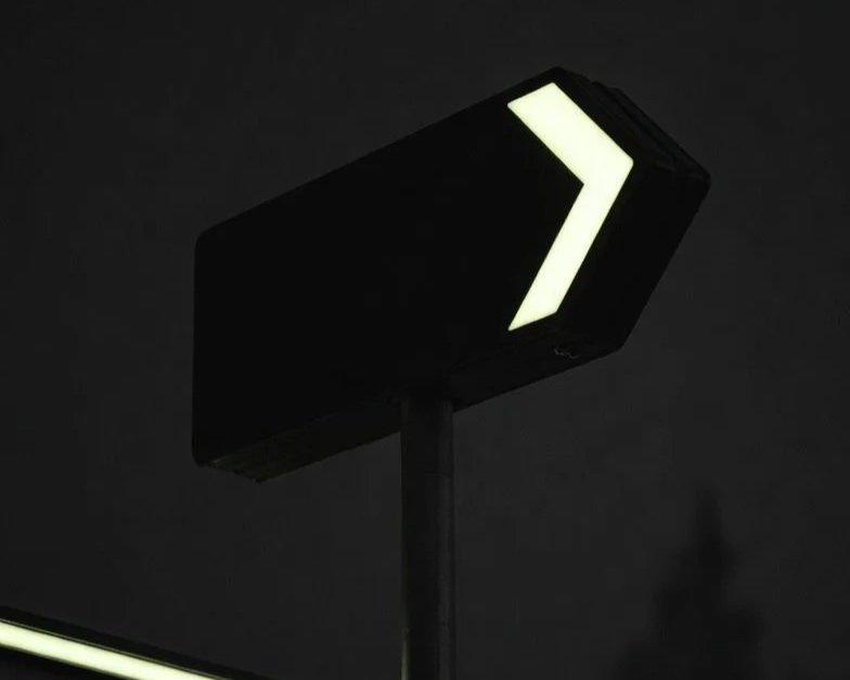 Panneau directionnel noir avec flèche lumineuse guidant les usagers de nuit