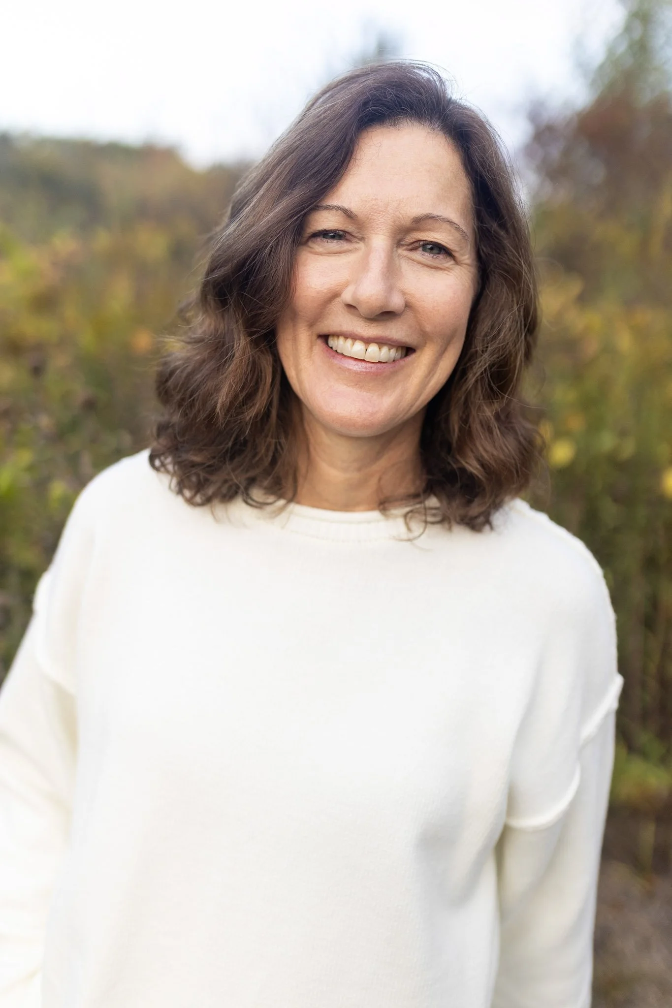 Author Debbie Prather with shoulder-length brown hair smiling outdoors with blurred trees in the background.