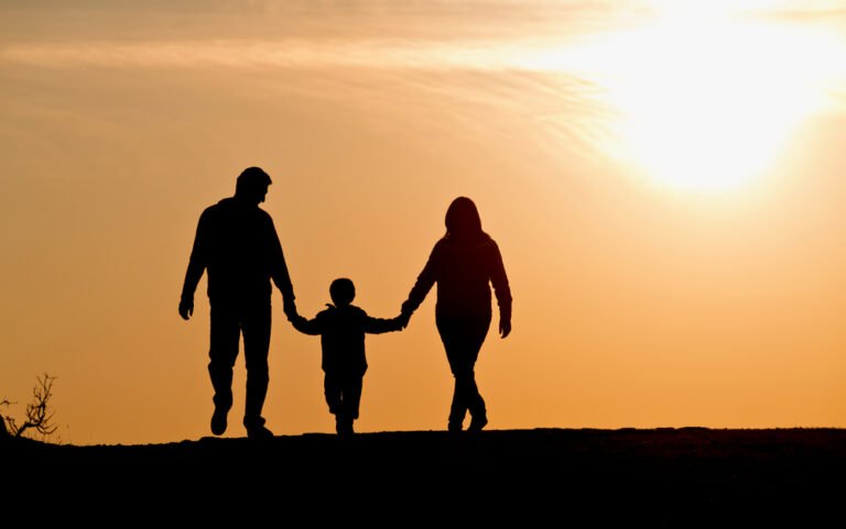 Silhouette of a family holding hands while walking outdoors during sunset.