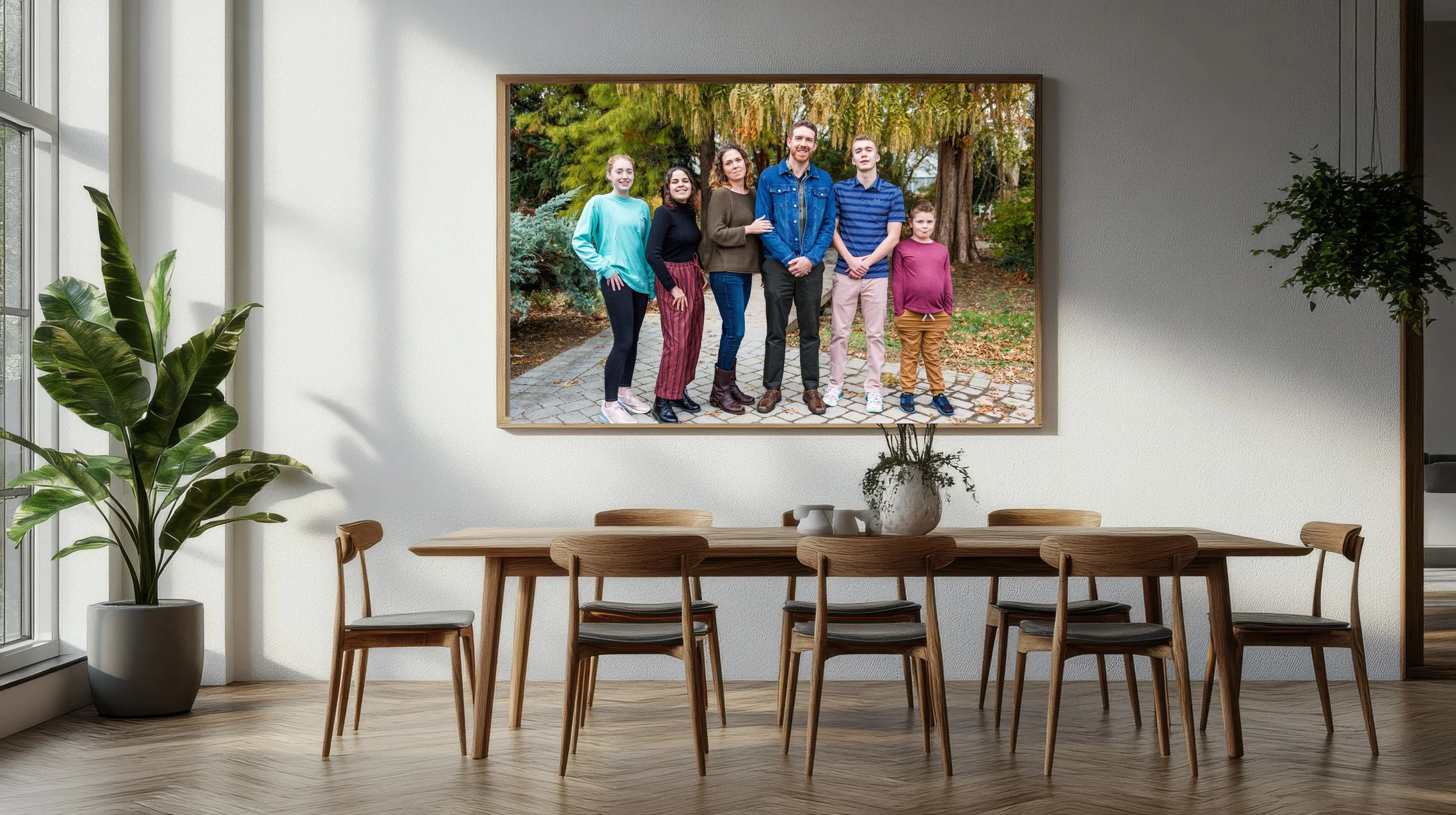 Large framed family photo hangs on white wall inside a dining room, showing six people outdoors with trees and leaves in fall colors.