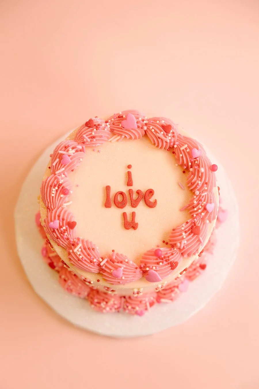 valentine desserts - round cake decorated with pink frosting and sprinkles with "i love u" written on it