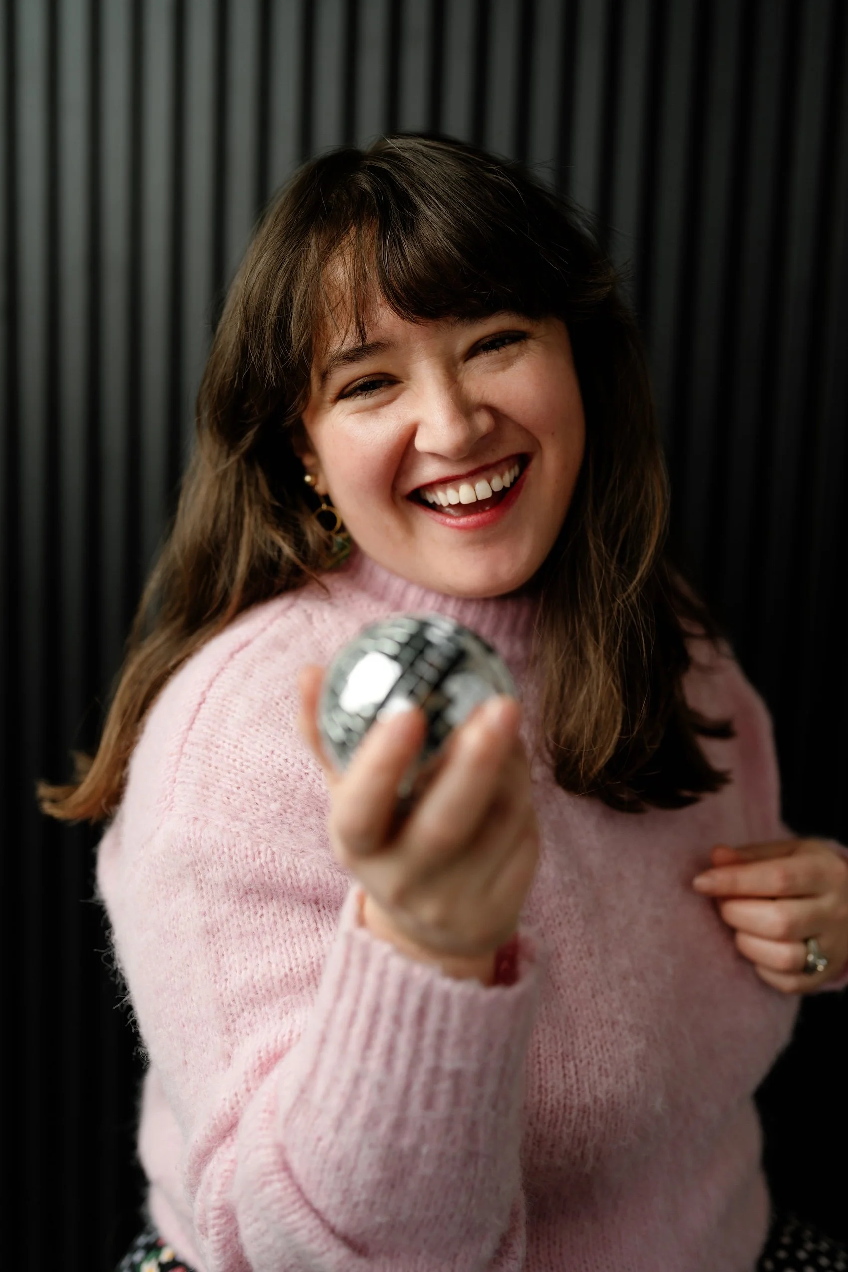 Headshot of ECBG Studio's team member, Yoli, holding a disco ball and smiling in pink sweater
