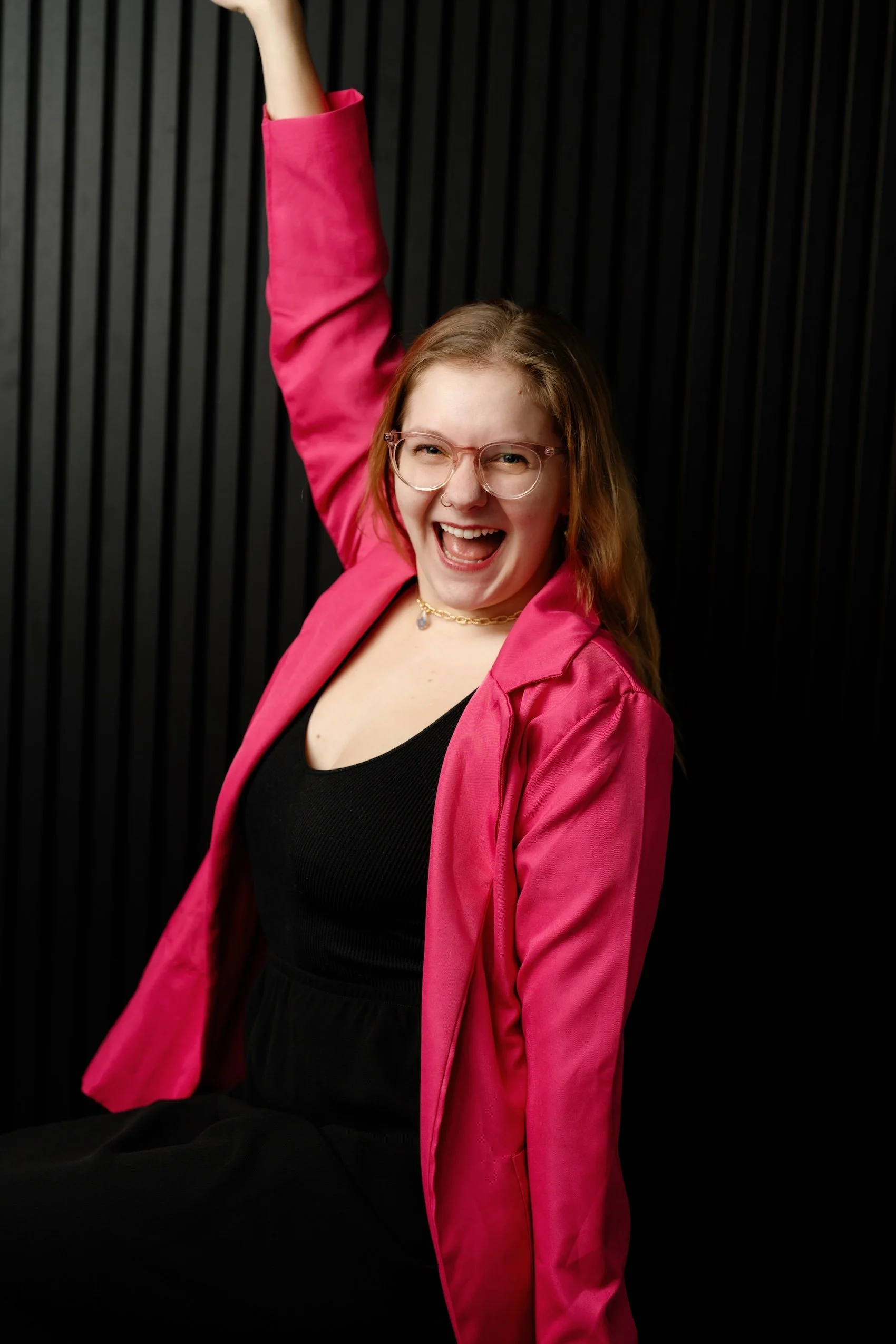 Headshot of ECBG Studio's team member, Izzy, raising arm up in pink blazer and smiling