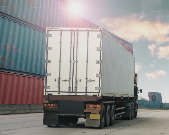 A large delivery truck on the highway with cargo containers stacked behind it under a bright sky.