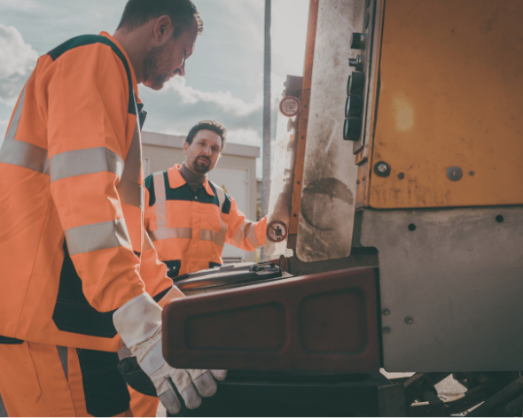 Two workers in orange safety uniforms inspecting machinery outdoors.