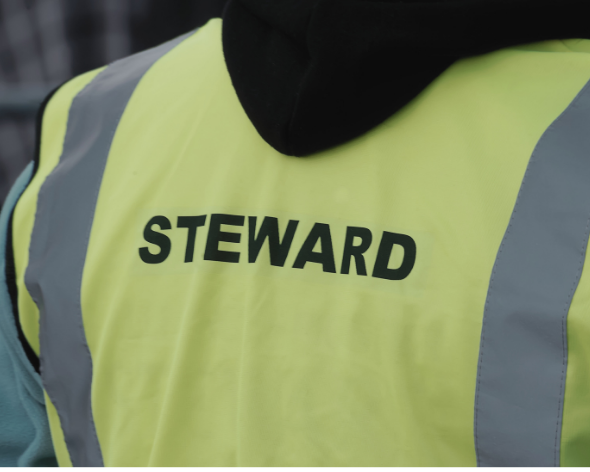 Close-up of a person's yellow high-visibility vest with the word 'STEWARD' printed on back.