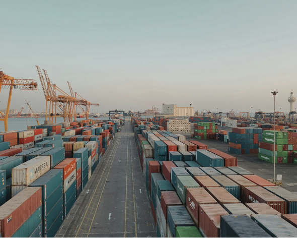 Large shipping port with numerous stacks of colorful cargo containers and cranes in the background.