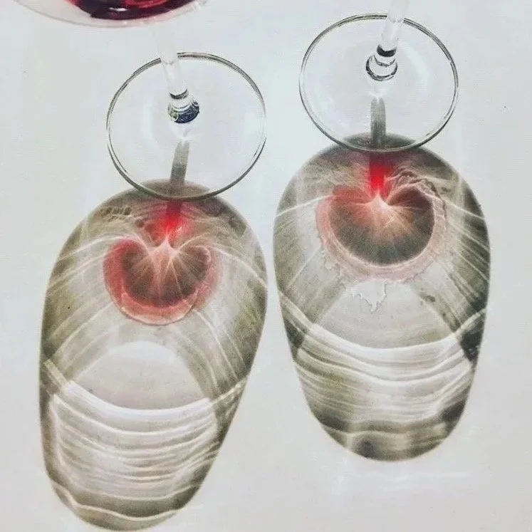 Two glasses of red wine placed upside down over polished stones with stripe patterns, creating the illusion of abstract faces with glowing red 'mouths' on a white surface.