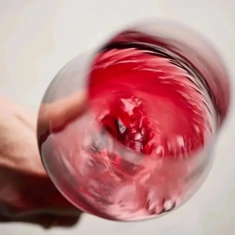 A hand holding a glass of red wine being swirled to create a blurred, swirling effect.