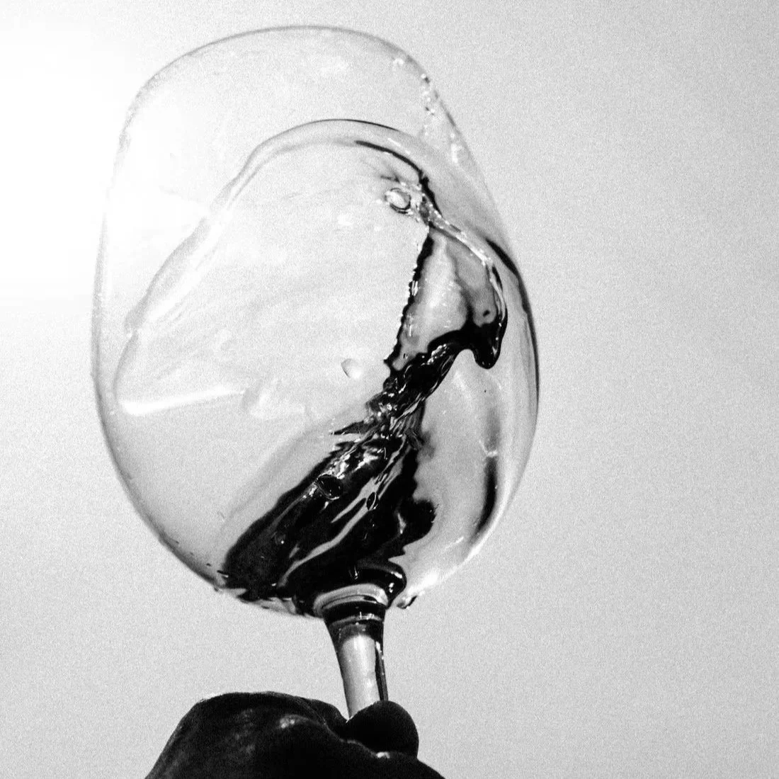 Black and white photo of a wine glass filled with water being held by a hand against a plain background.