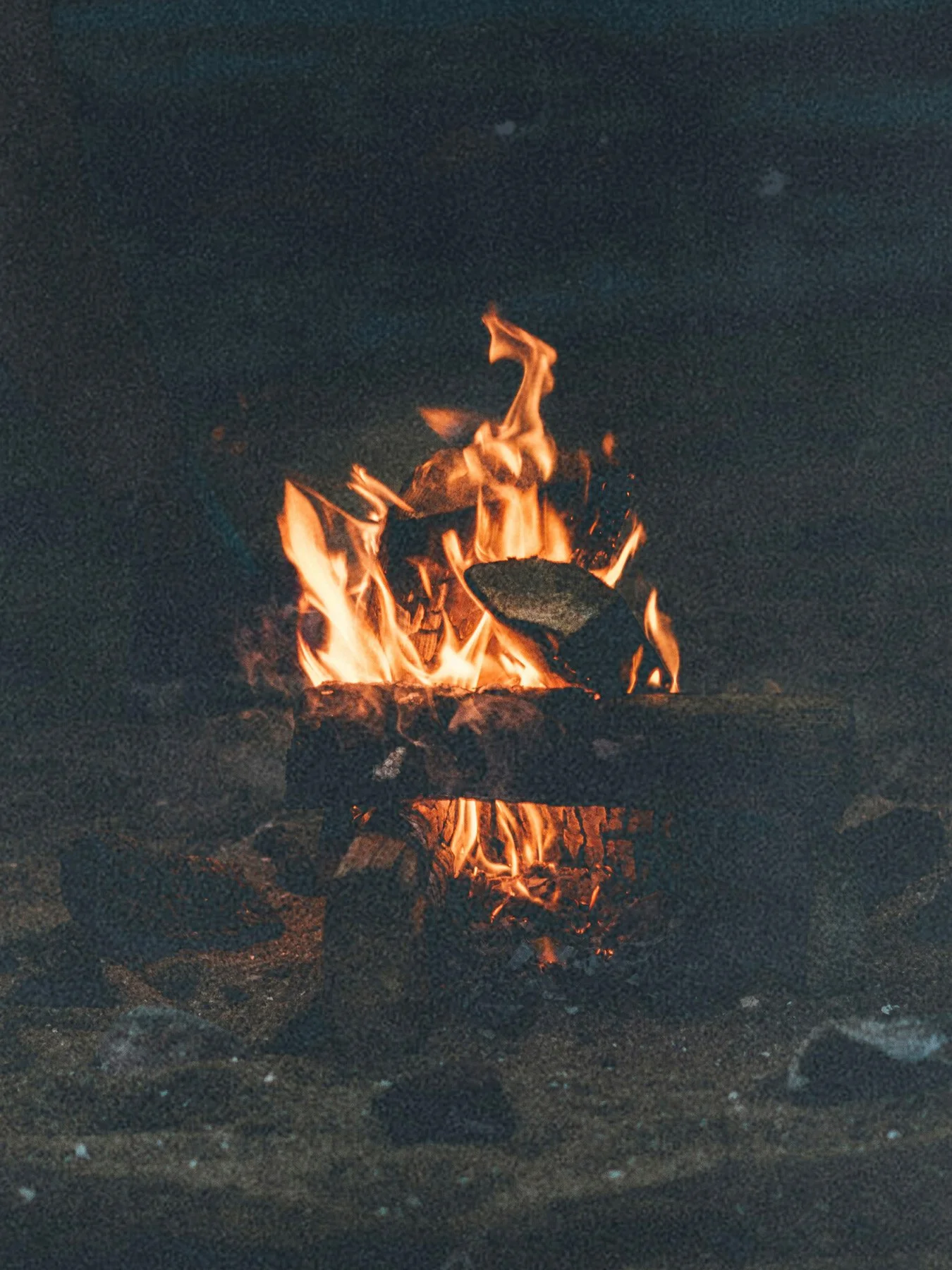 Campfire burning on sandy ground at night.