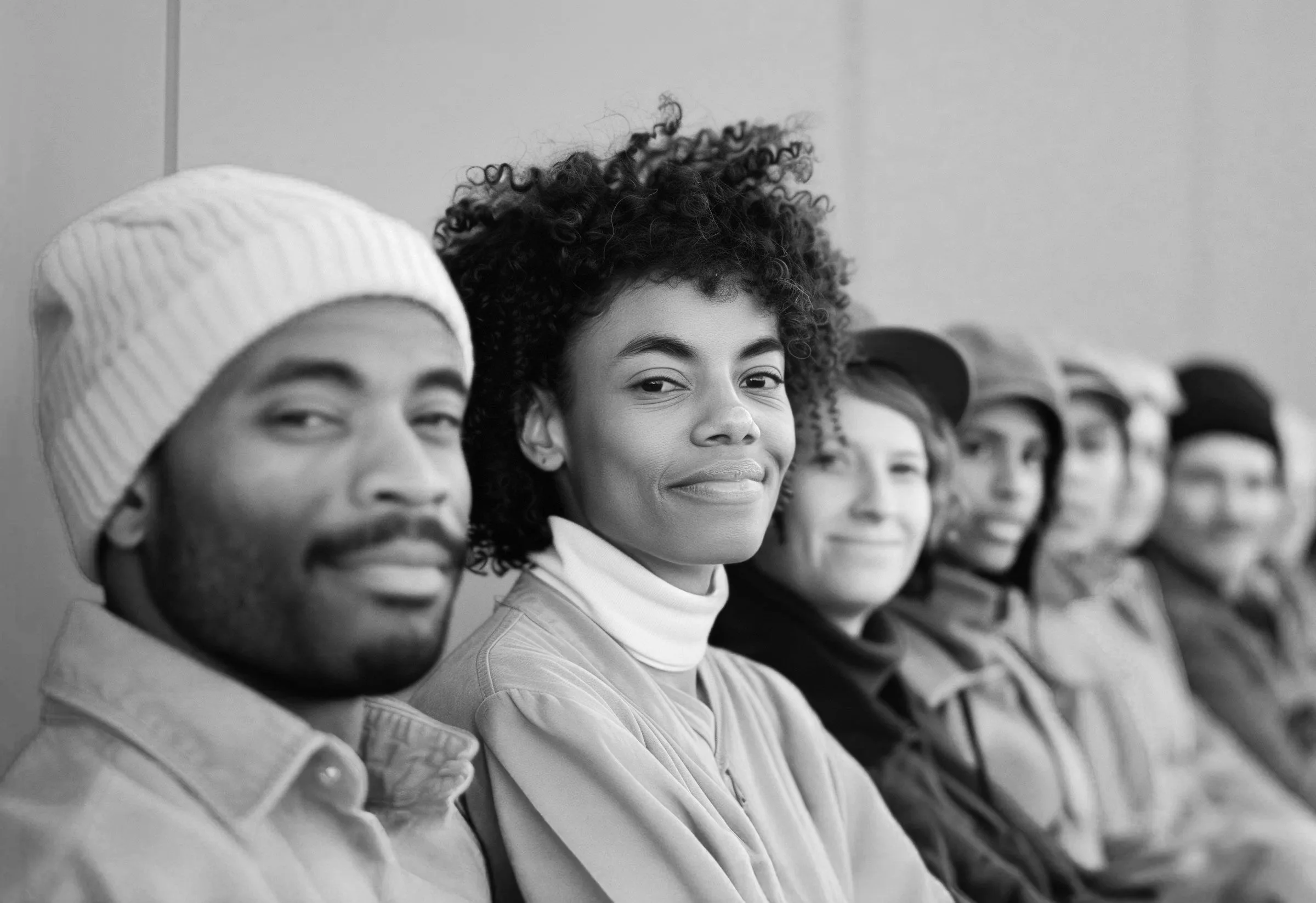 Line of diverse young adults sitting in a row, smiling, black and white photo.