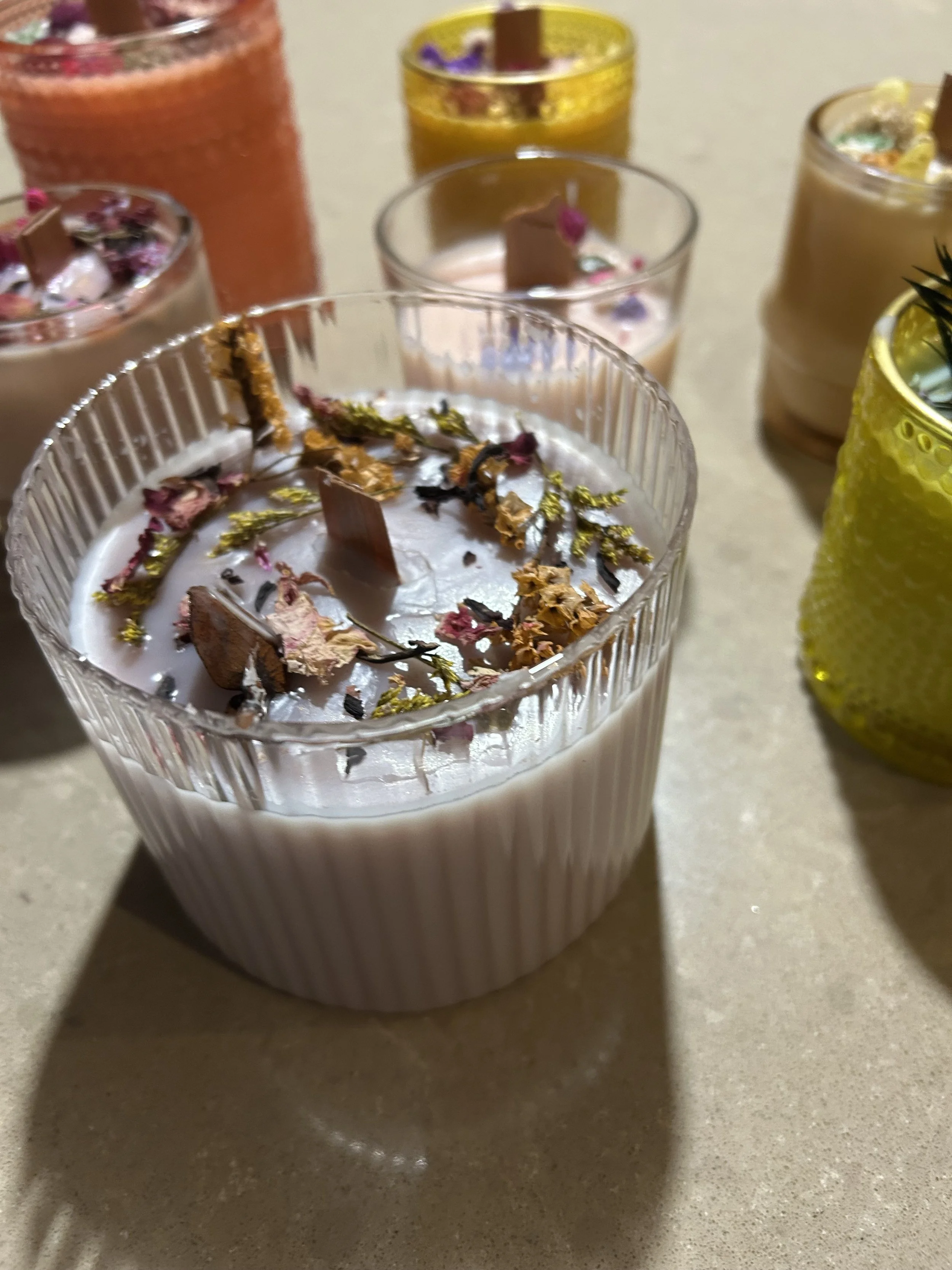 Vier geverfde kaarsen met houten lonten, geplaatst op een houten snijplank met touw en een schaar ernaast.