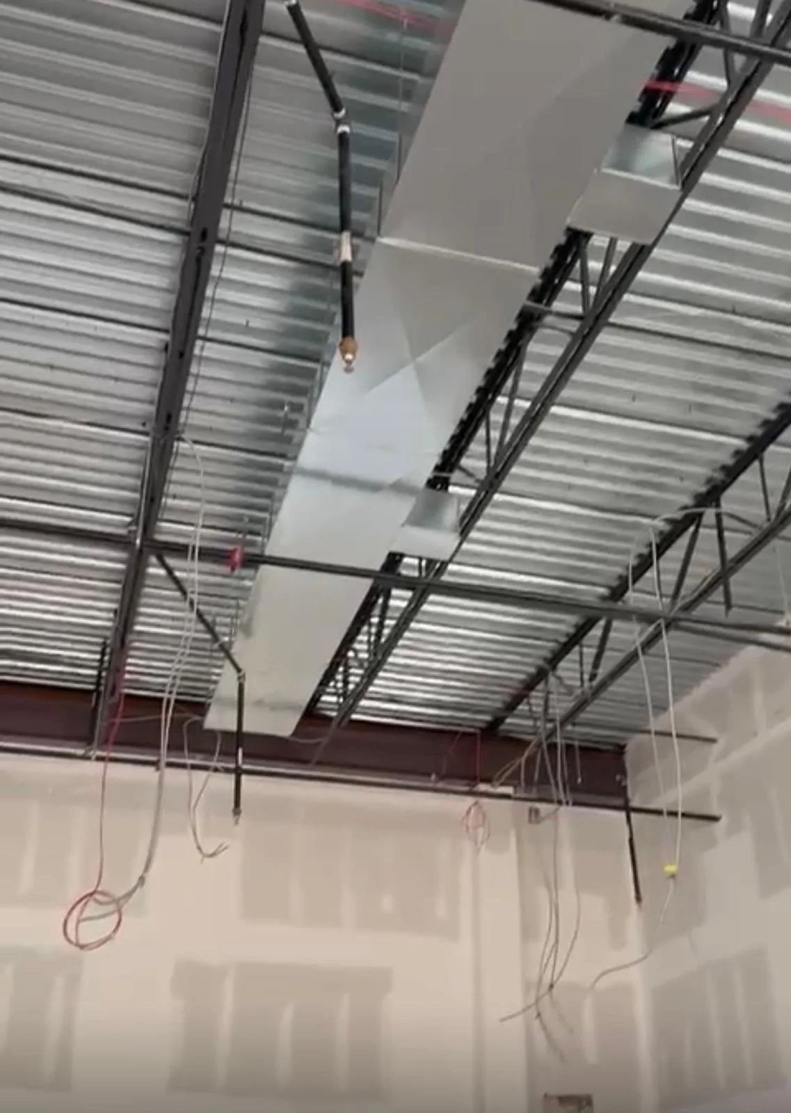 Construction ceiling with metal framing, ductwork, and electrical wiring hanging from the ceiling.