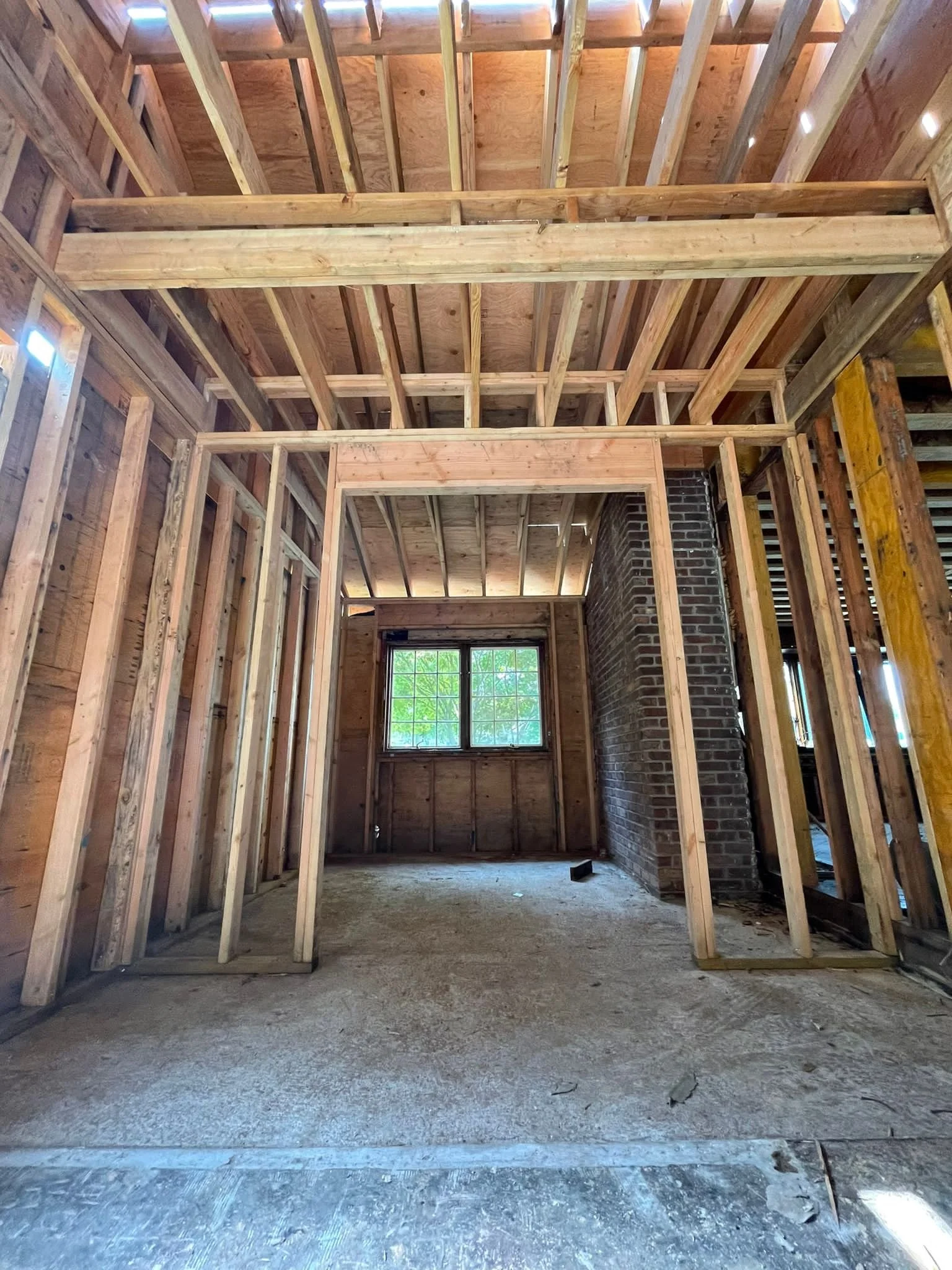 Interior of a building under construction with exposed wooden framing, a brick chimney, and a window at the back.