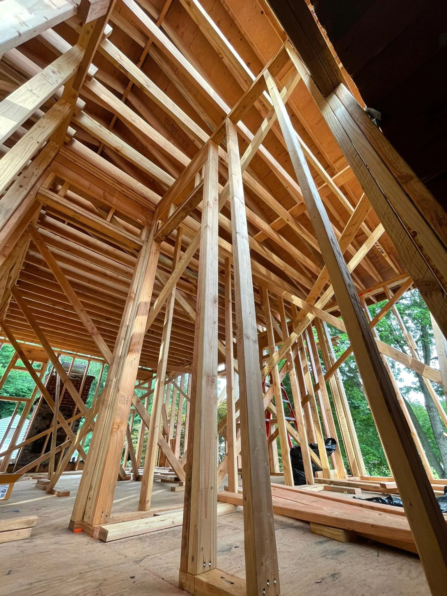 Interior view of a house under construction, showing wooden framing for walls and ceiling, with some framing braces, a ladder, and construction materials.