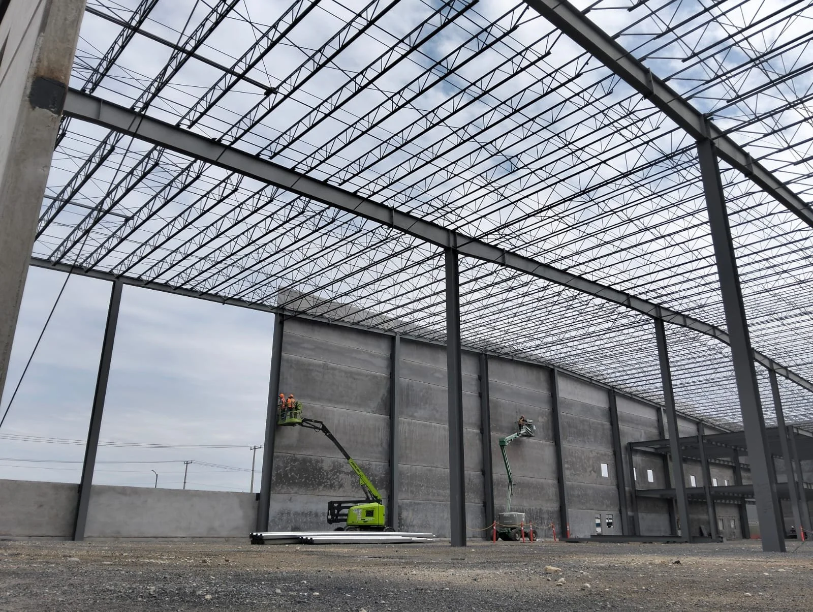 Construcción de nave industrial de muros precolados en concreto en un parque industrial, con maquinaria especializada y trabajadores en uso de equipo de protección personal.