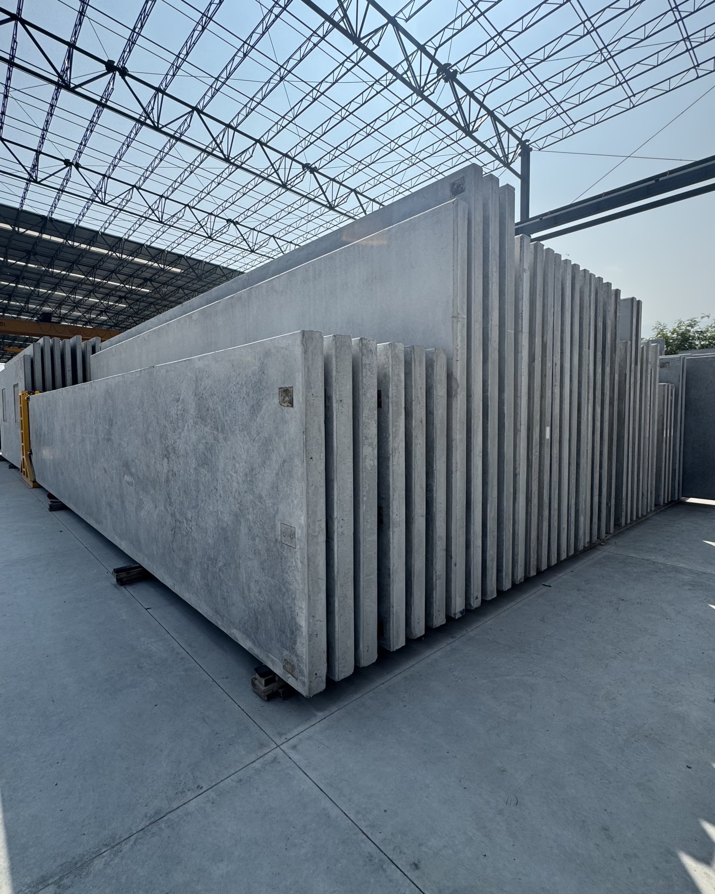 Large concrete slabs stacked in an outdoor industrial setting with a steel framework roof above.