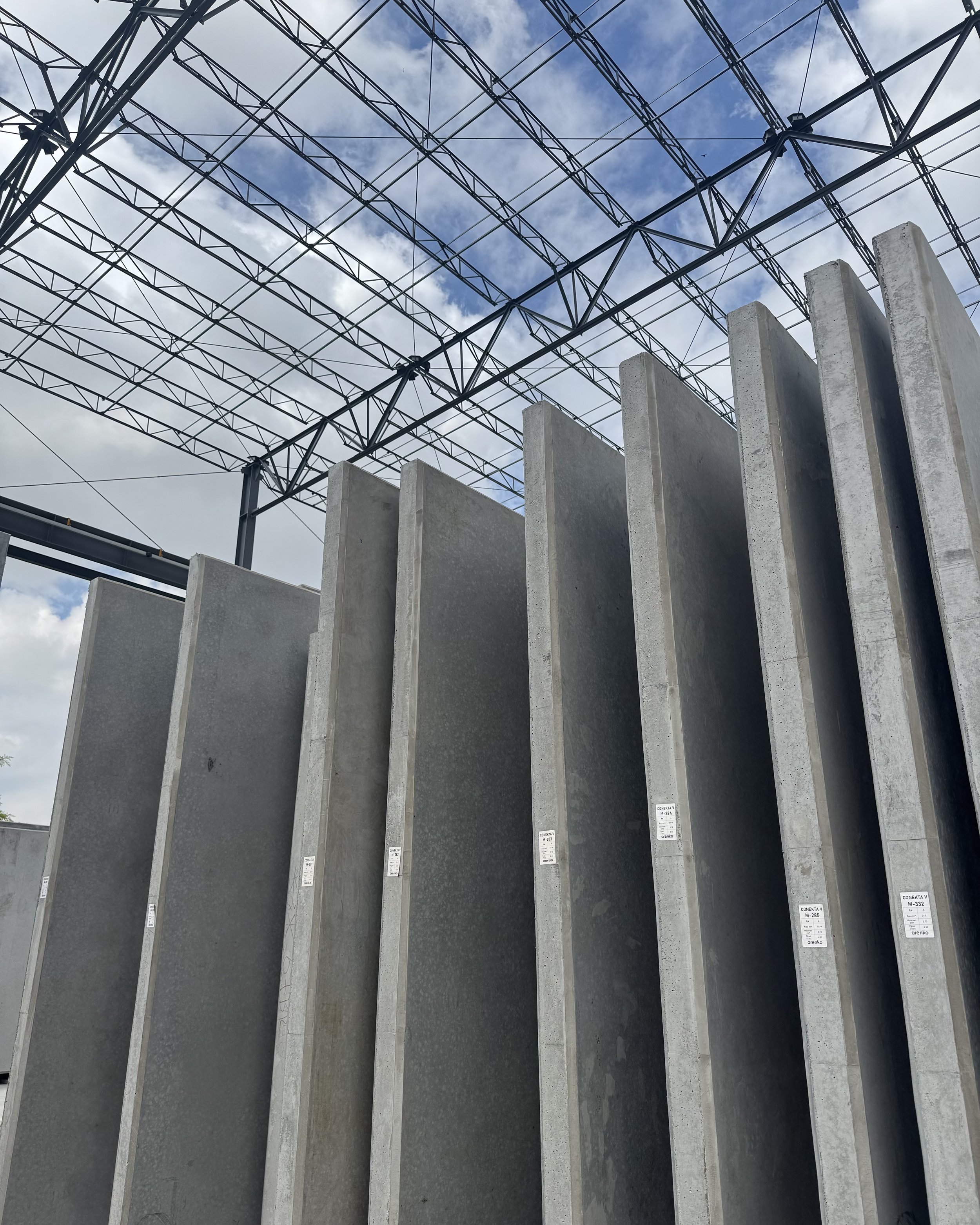 Vertical concrete slabs stacked outdoors under a cloudy sky with metal scaffolding overhead.