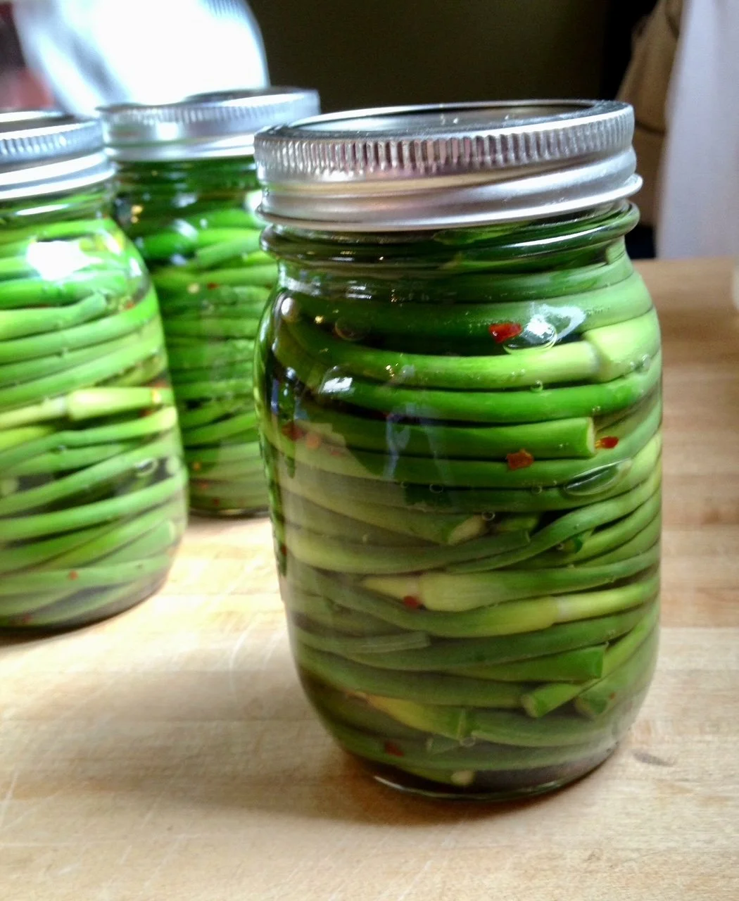 Jars filled with green beans submerged in pickling liquid, stored on a wooden surface.