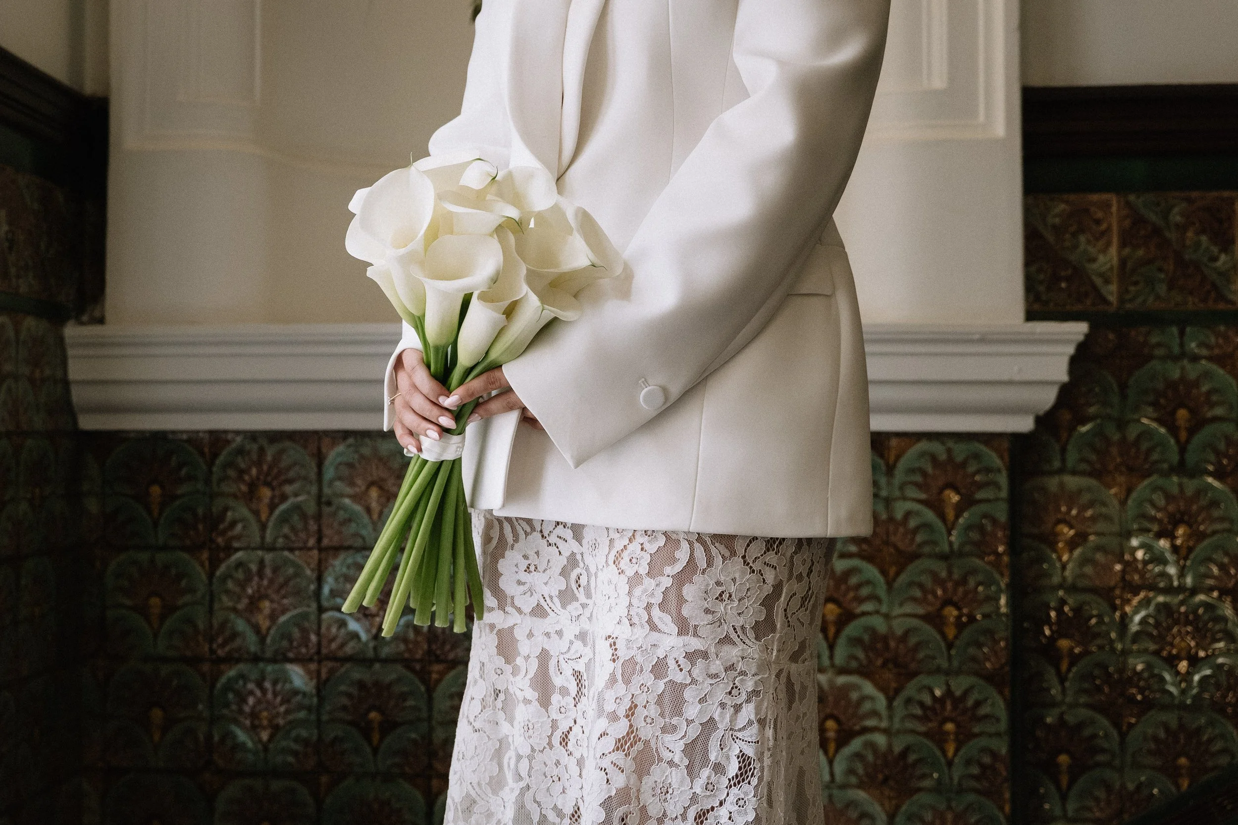 A person in a white suit jacket and a lace skirt holding a bouquet of white calla lilies. - captured by an Edinburgh wedding photographer