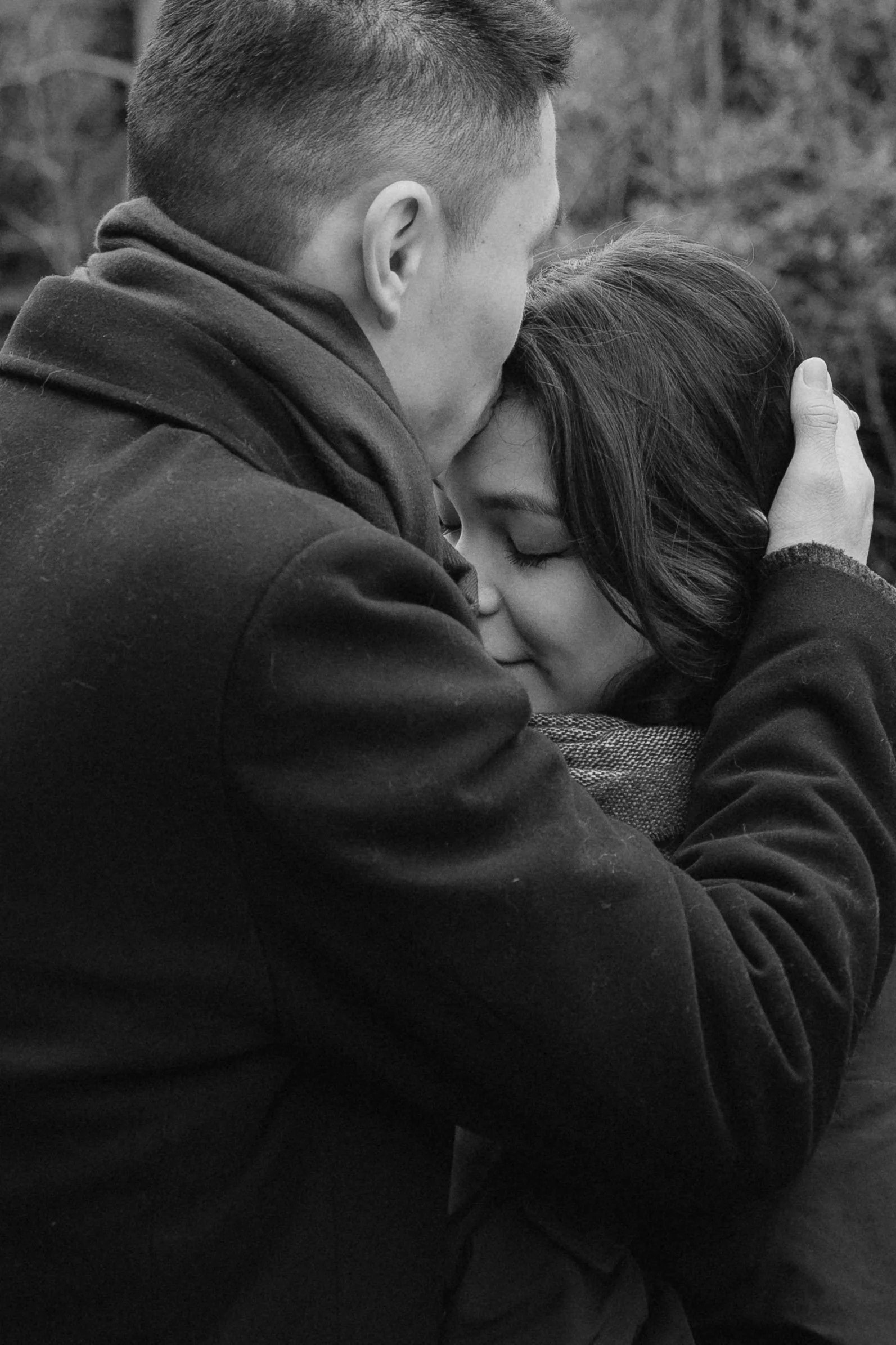 A man and a woman embracing warmly, with the man kissing the woman's forehead as she closes her eyes, outdoors in a natural setting. - captured by an Edinburgh wedding photographer