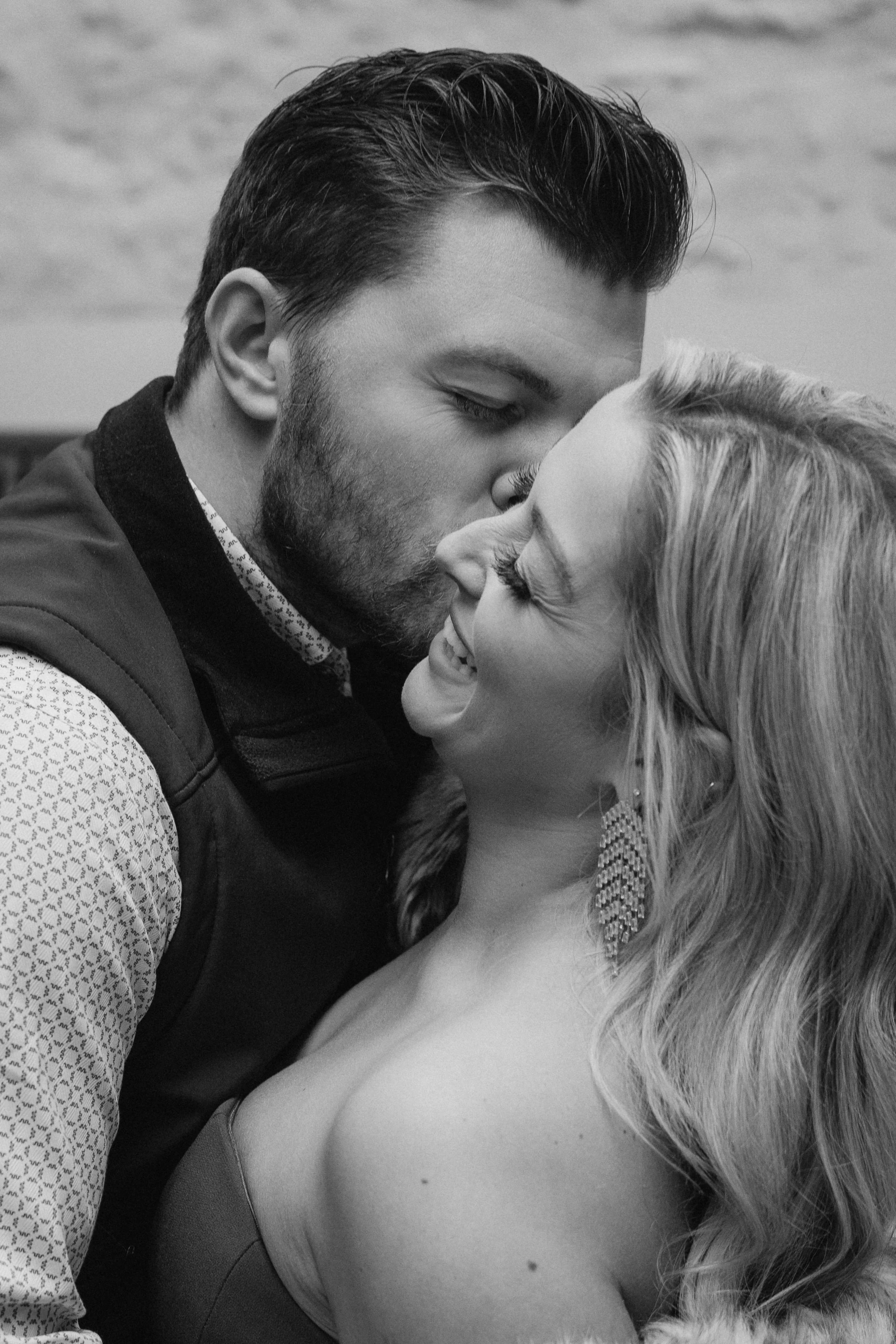 A black and white photo of a man and woman sharing a kiss, with the man about to kiss the woman on her nose and the woman smiling with her eyes partly closed. - captured by an Edinburgh wedding photographer