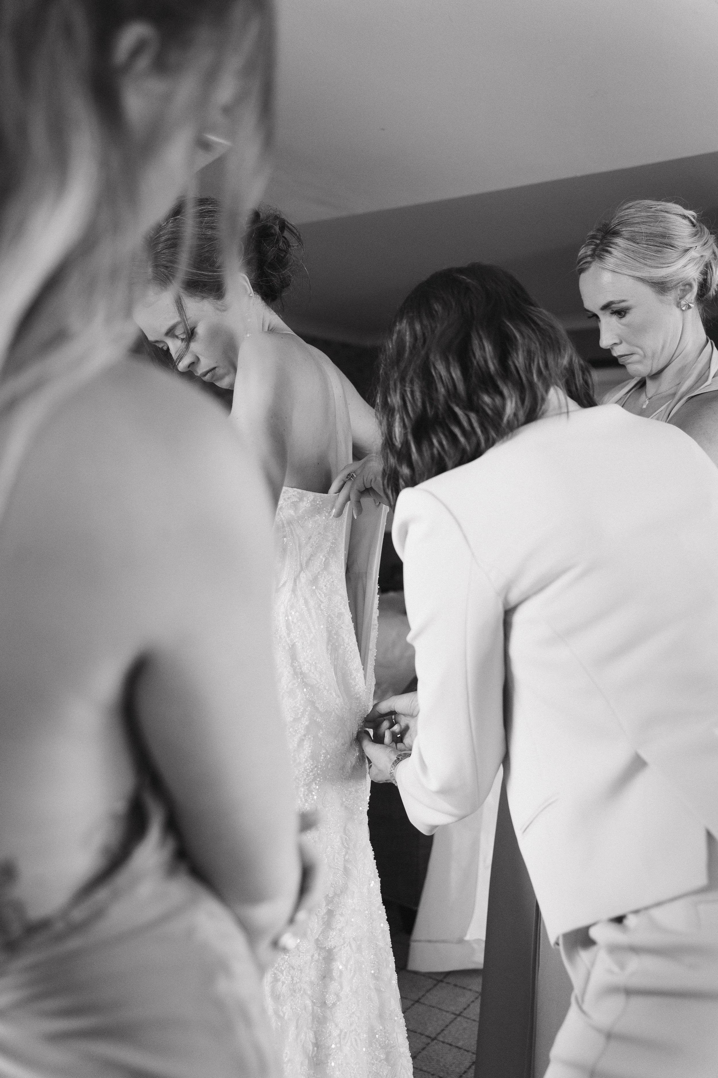 Women helping bride put on wedding dress in a dressing room. - captured by an Edinburgh wedding photographer