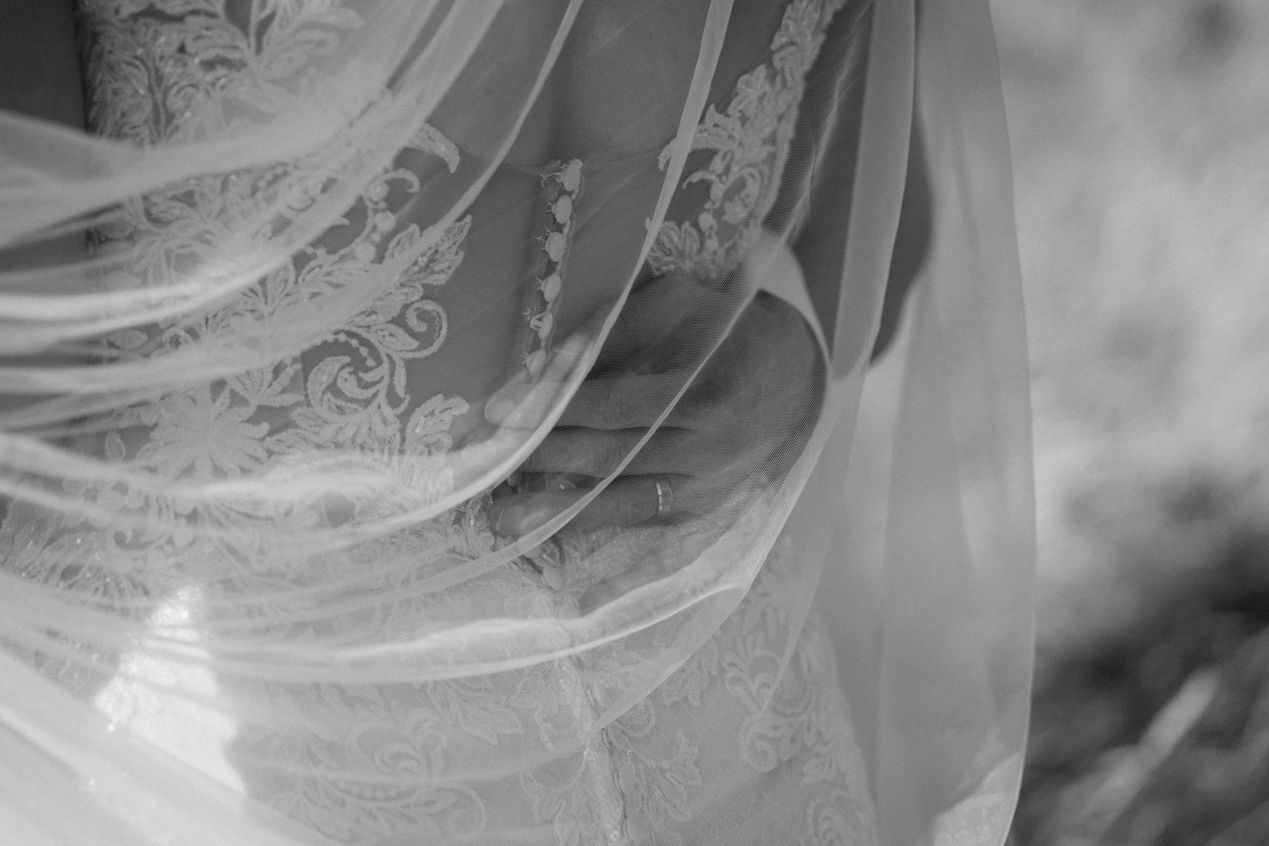 Close-up of a bride's hand with a ring, partially covered by a sheer lace veil with floral embroidery, on her wedding dress. - captured by an Edinburgh wedding photographer