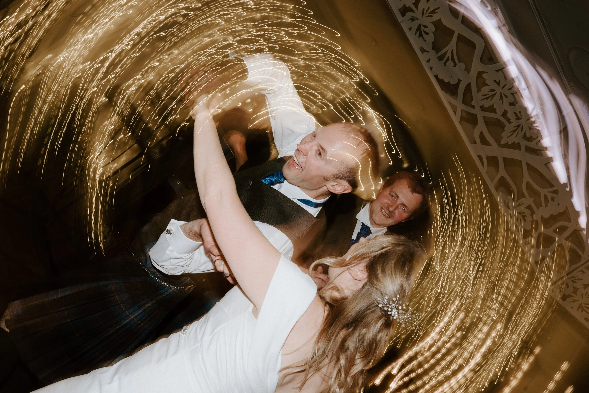 People dancing at a wedding reception with swirling lights around them. - captured by an Edinburgh wedding photographer