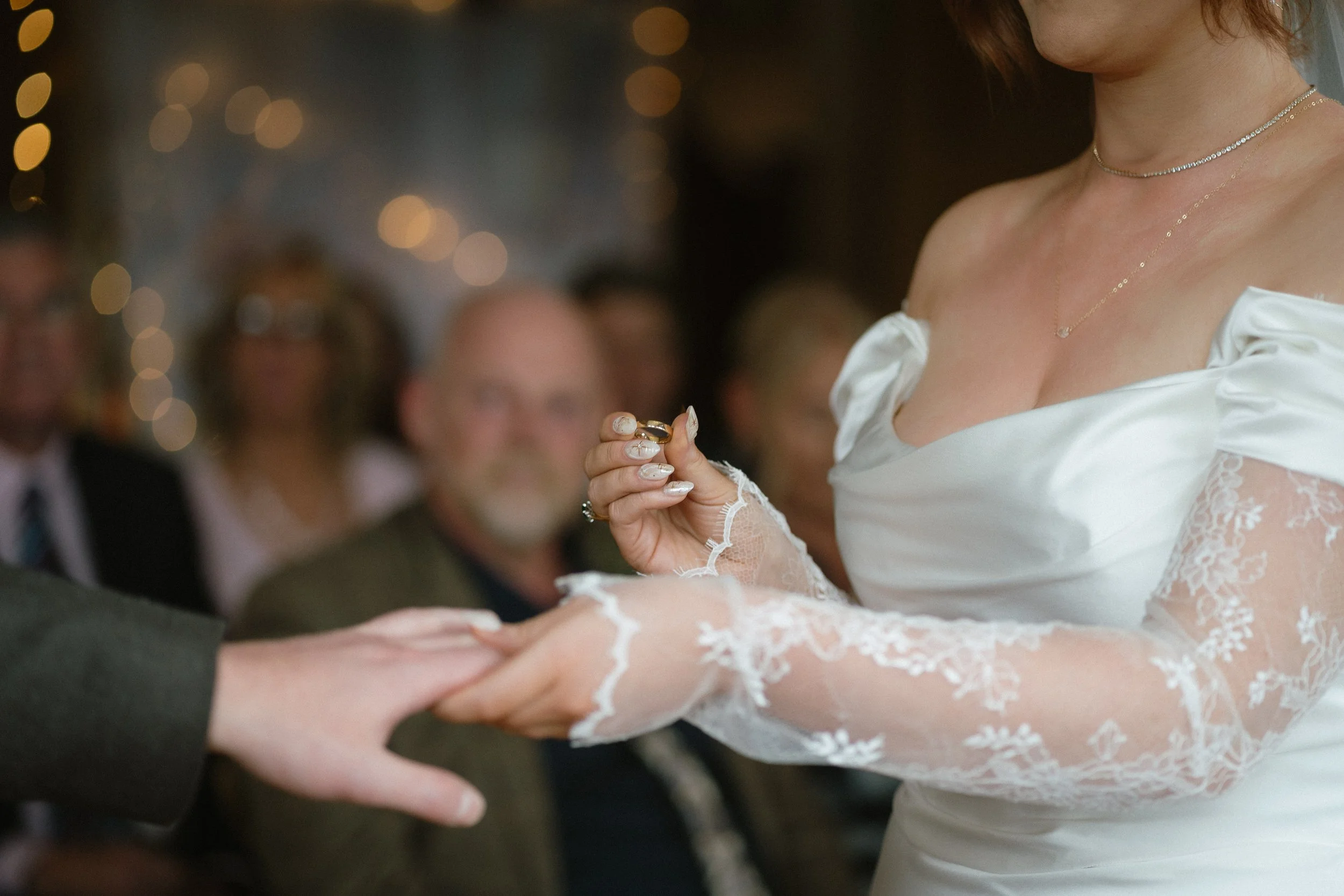 A bride exchanging wedding rings with a groom during a wedding ceremony, with guests watching in the background. - captured by an Edinburgh wedding photographer