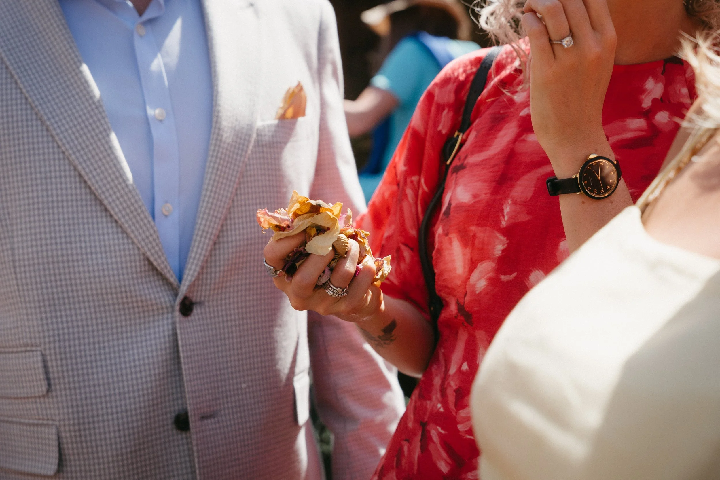 People in formal attire at an outdoor event, one person holding a sandwich or snack, with focus on their hands and clothing. - captured by an Edinburgh wedding photographer