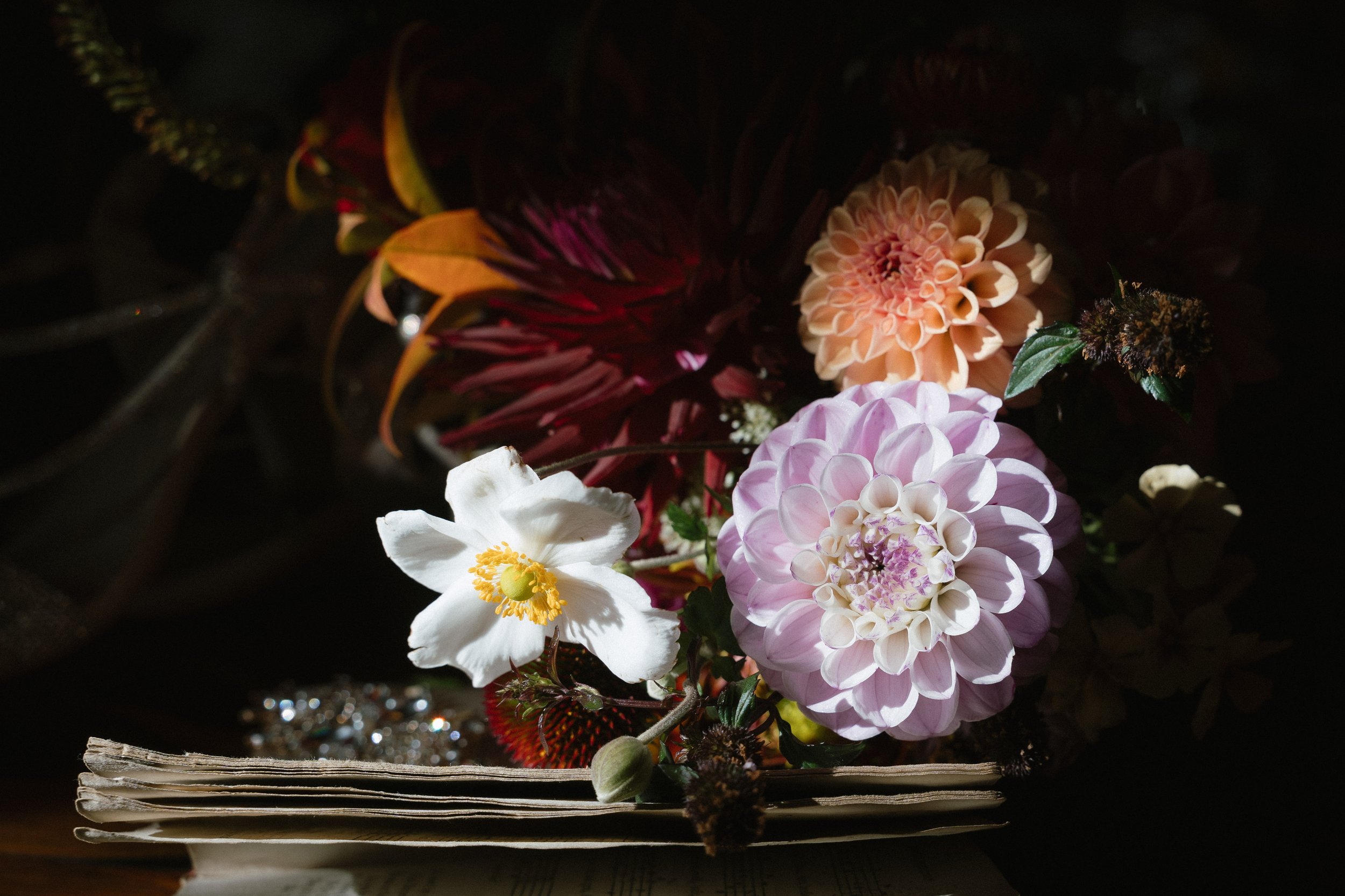 A bouquet of various flowers including a white flower with a yellow center, peach-colored, pink, and red flowers, arranged on top of a folded newspaper with a dark background. - captured by an Edinburgh wedding photographer