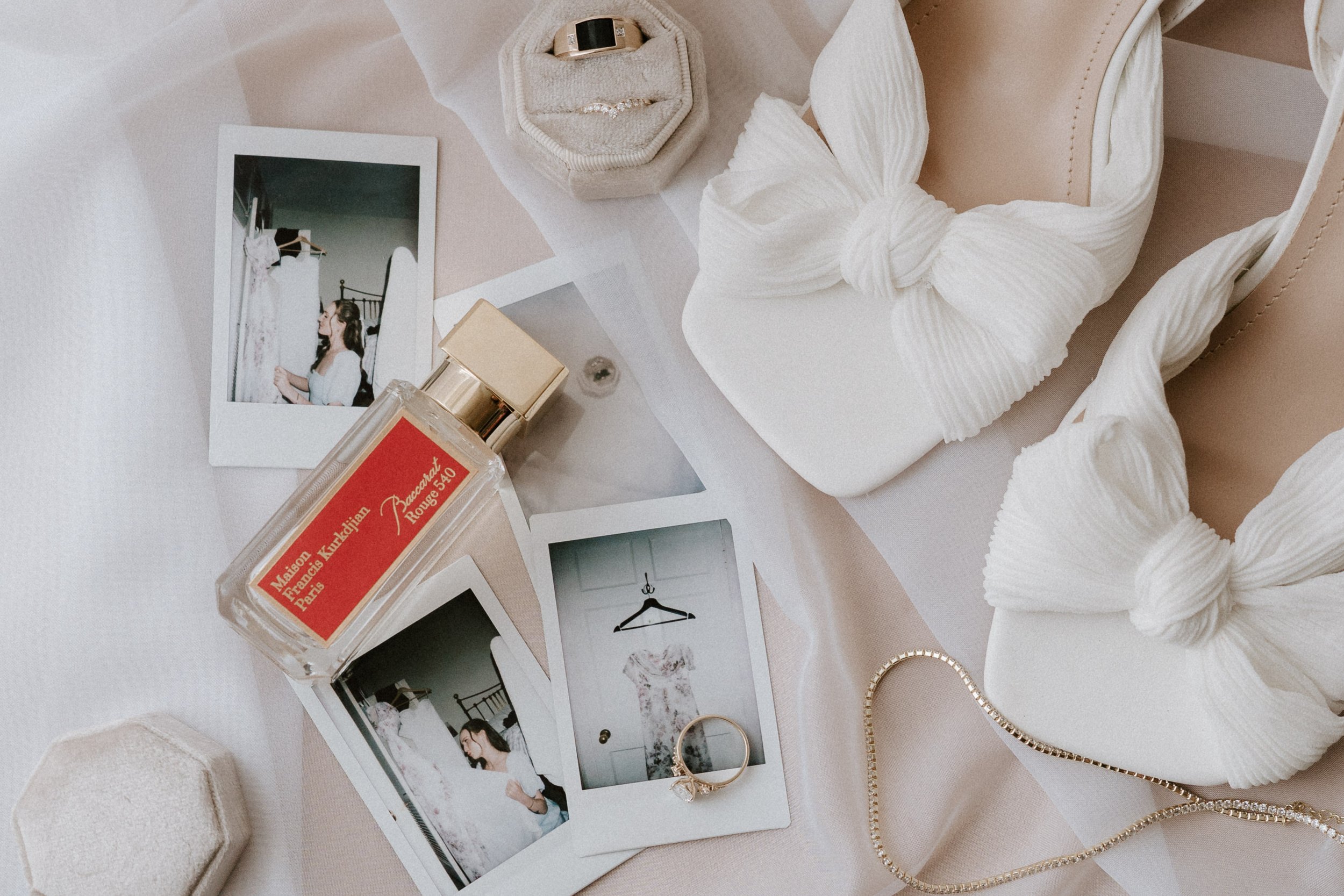 Various jewelry, photos, a perfume bottle, a pair of white shoes with bows, and a ring, arranged on a light-colored surface. - captured by an Edinburgh wedding photographer