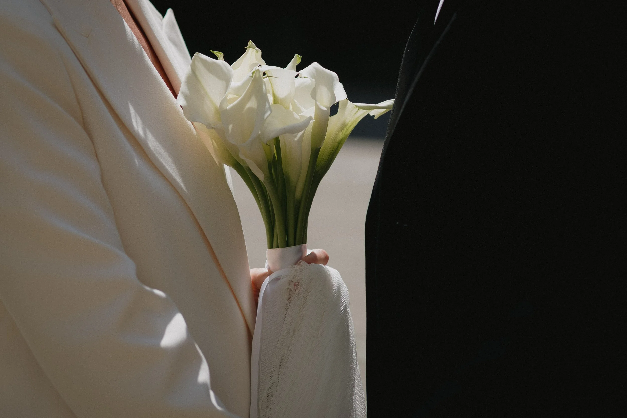 Person in a cream-colored suit holding a bouquet of white calla lilies - captured by an Edinburgh wedding photographer