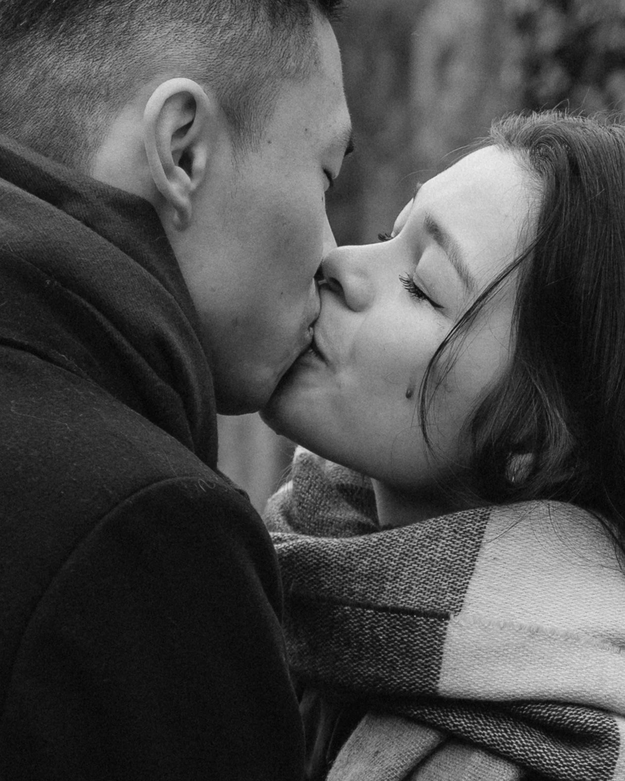 A black and white photo of a couple sharing a kiss with their eyes closed, the woman is wearing a plaid scarf - captured by an Edinburgh wedding photographer