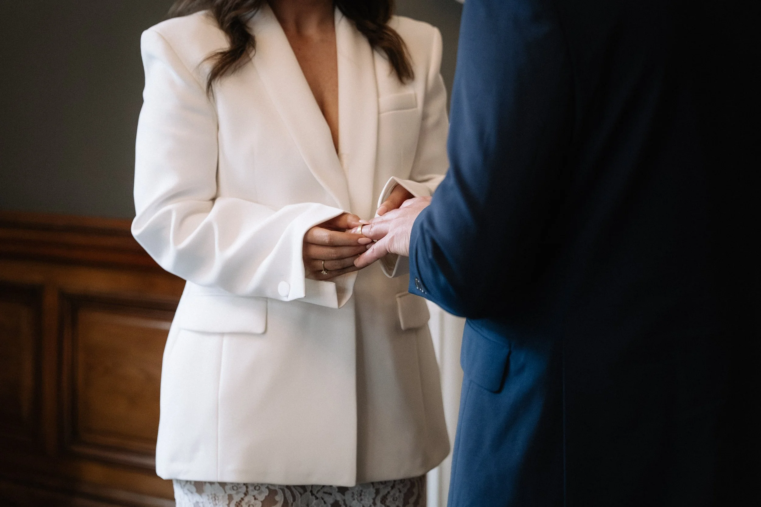 A woman in a white blazer and lace dress holding hands of a man in a navy suit during a wedding ceremony. - captured by an Edinburgh wedding photographer