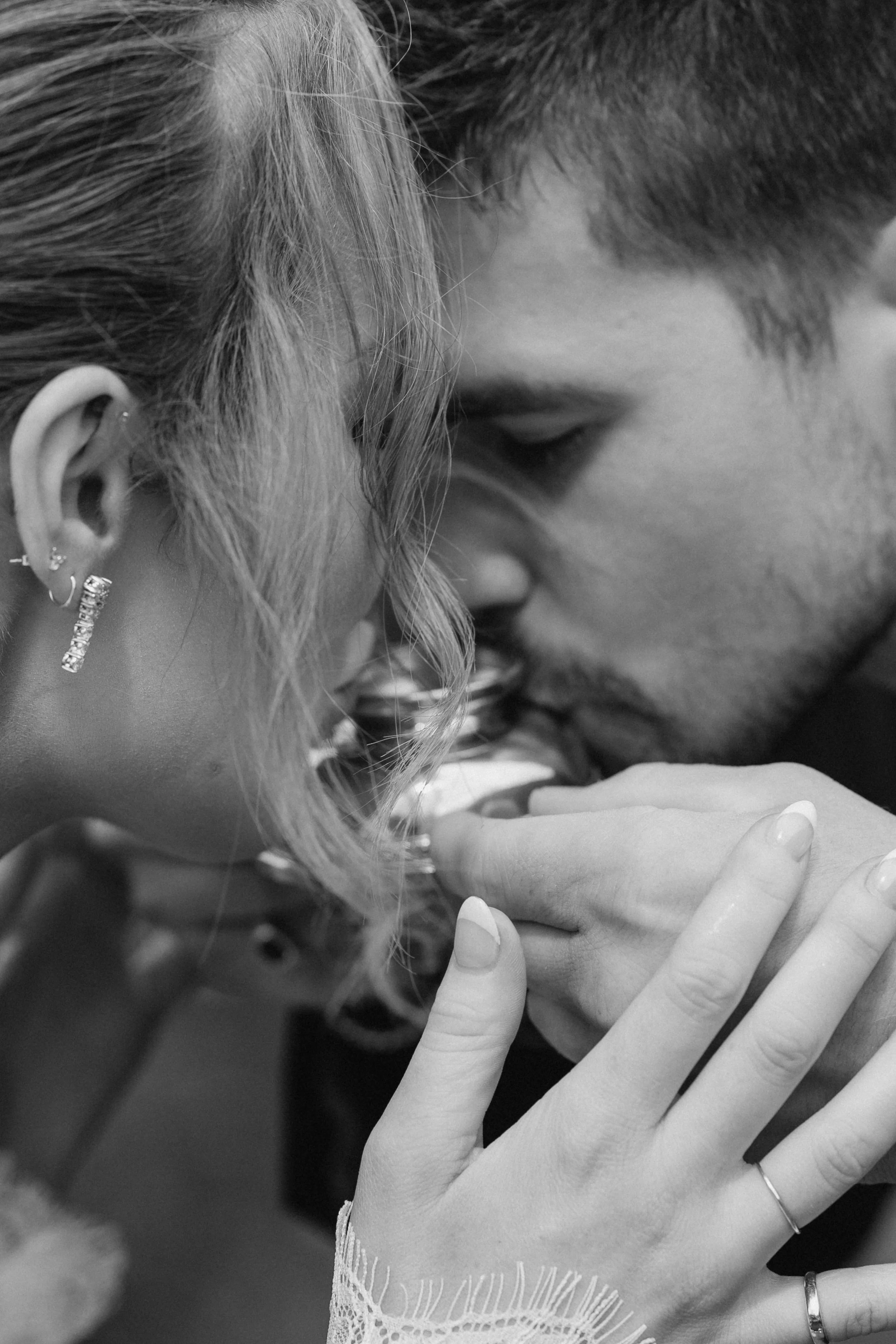A close-up black and white photo of a couple touching foreheads and holding hands, with the woman's hand displaying rings and an earring, and the man gently touching her hand. - captured by an Edinburgh wedding photographer