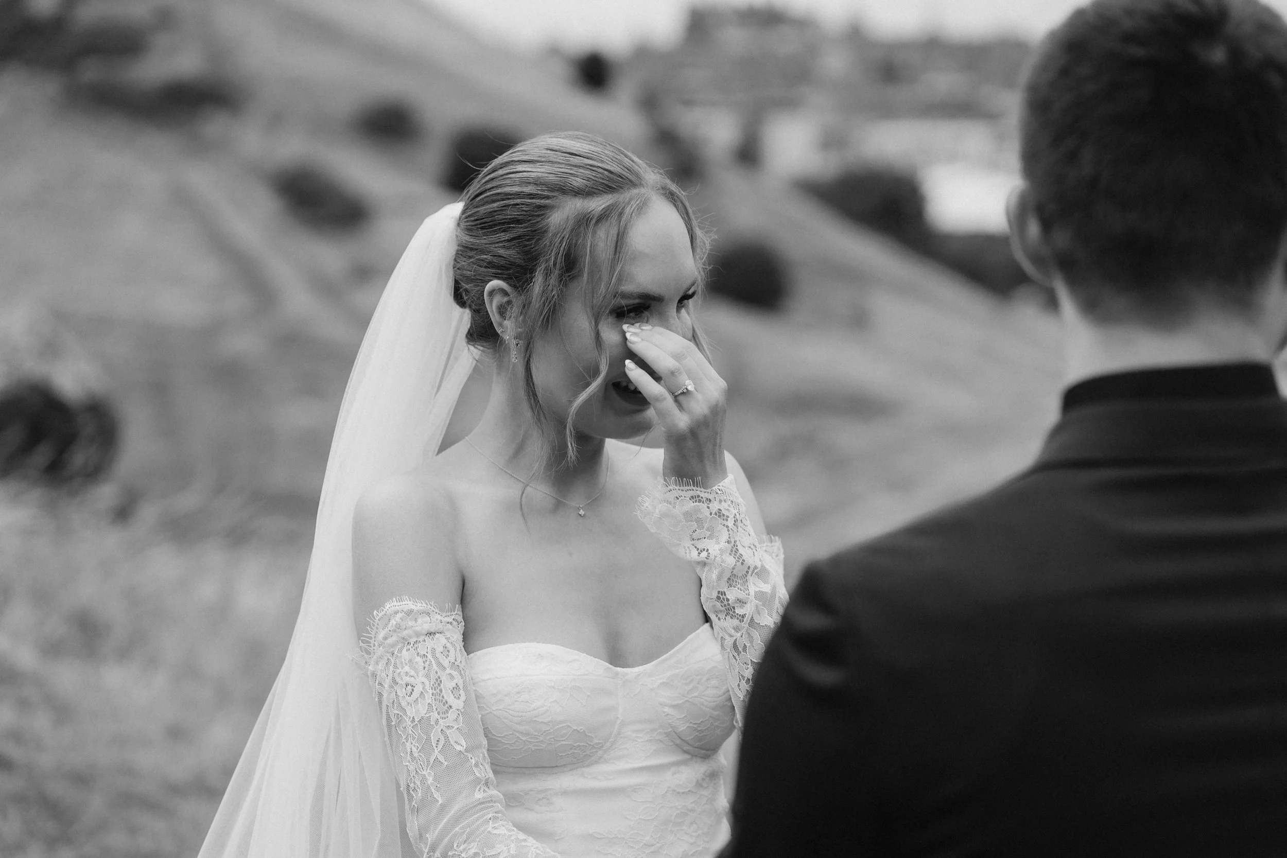 A bride crying during her wedding ceremony outdoors, with a groom facing her, on a grassy hillside. - captured by an Edinburgh wedding photographer