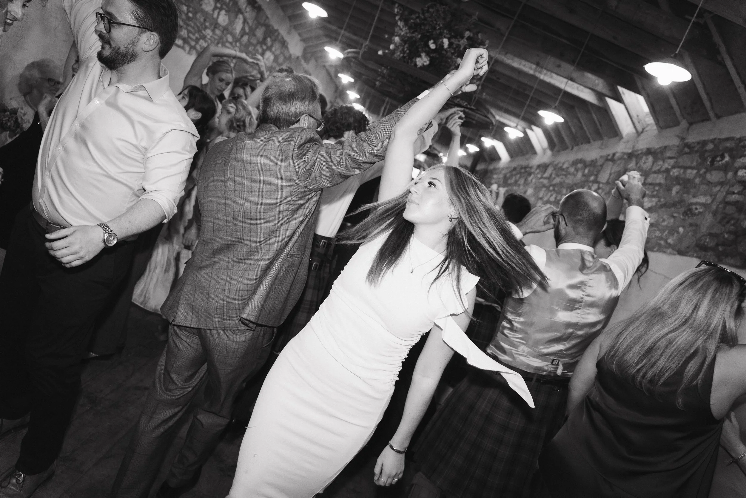 People dancing in a dimly lit indoor venue with stone walls and wooden ceiling, enjoying the music. - captured by an Edinburgh wedding photographer