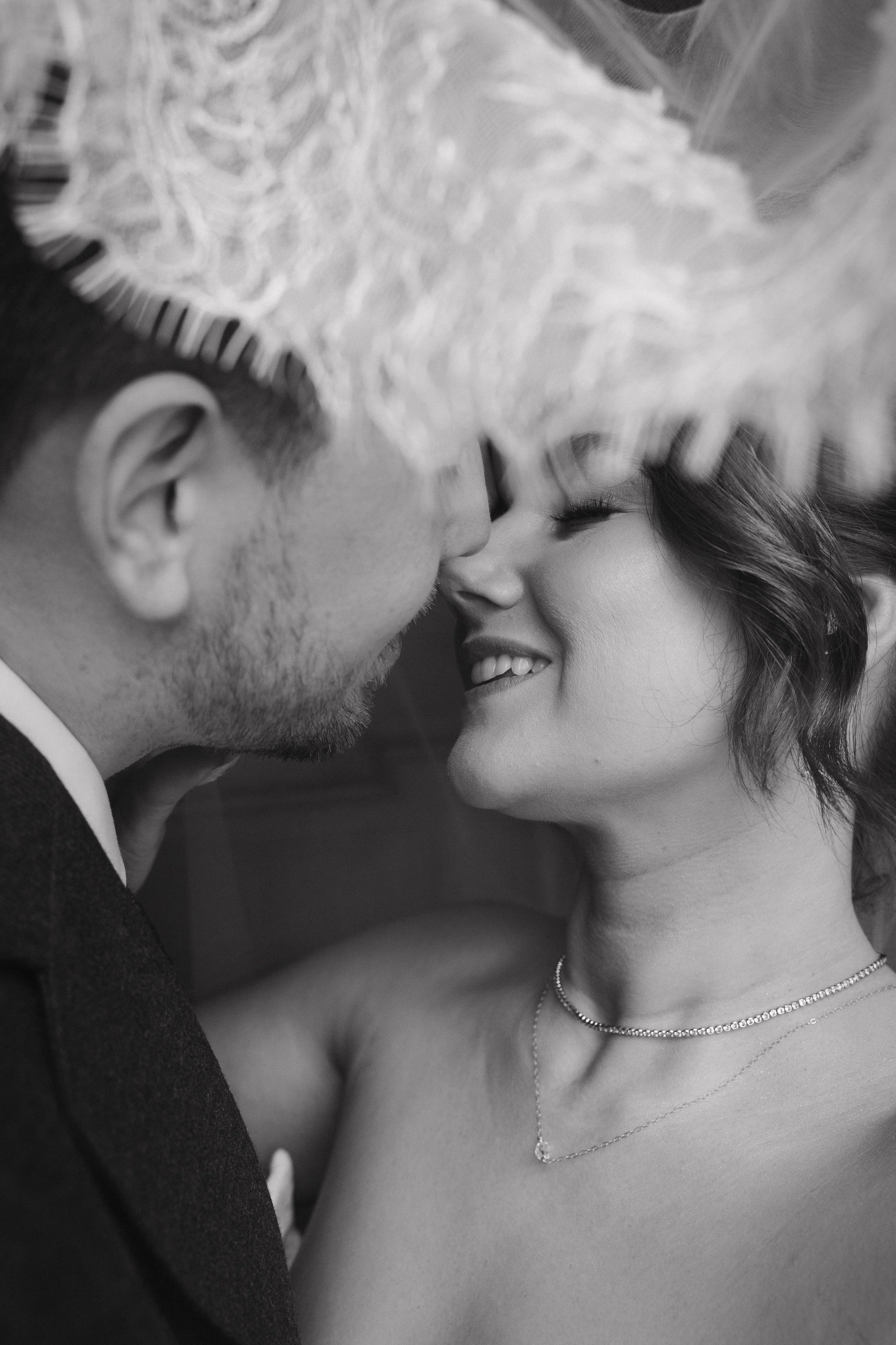 A close-up black and white photo of a couple about to kiss, with the woman smiling softly, their faces close together in an intimate moment. - captured by an Edinburgh wedding photographer