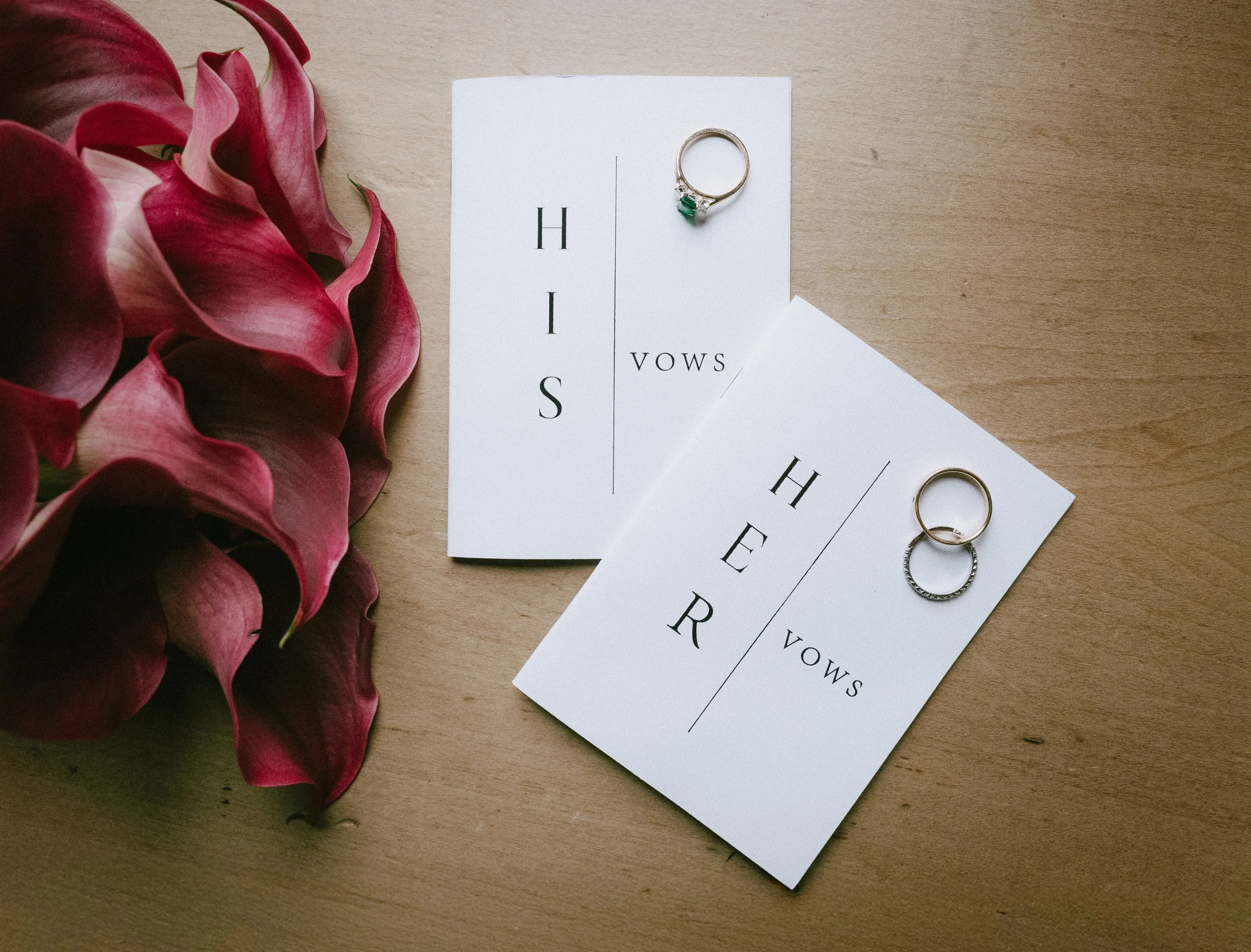 Two cards, one with the word 'HIS' and the other with the word 'HER', each with a vow written underneath, accompanied by a pink flower on a wooden surface. - captured by an Edinburgh wedding photographer