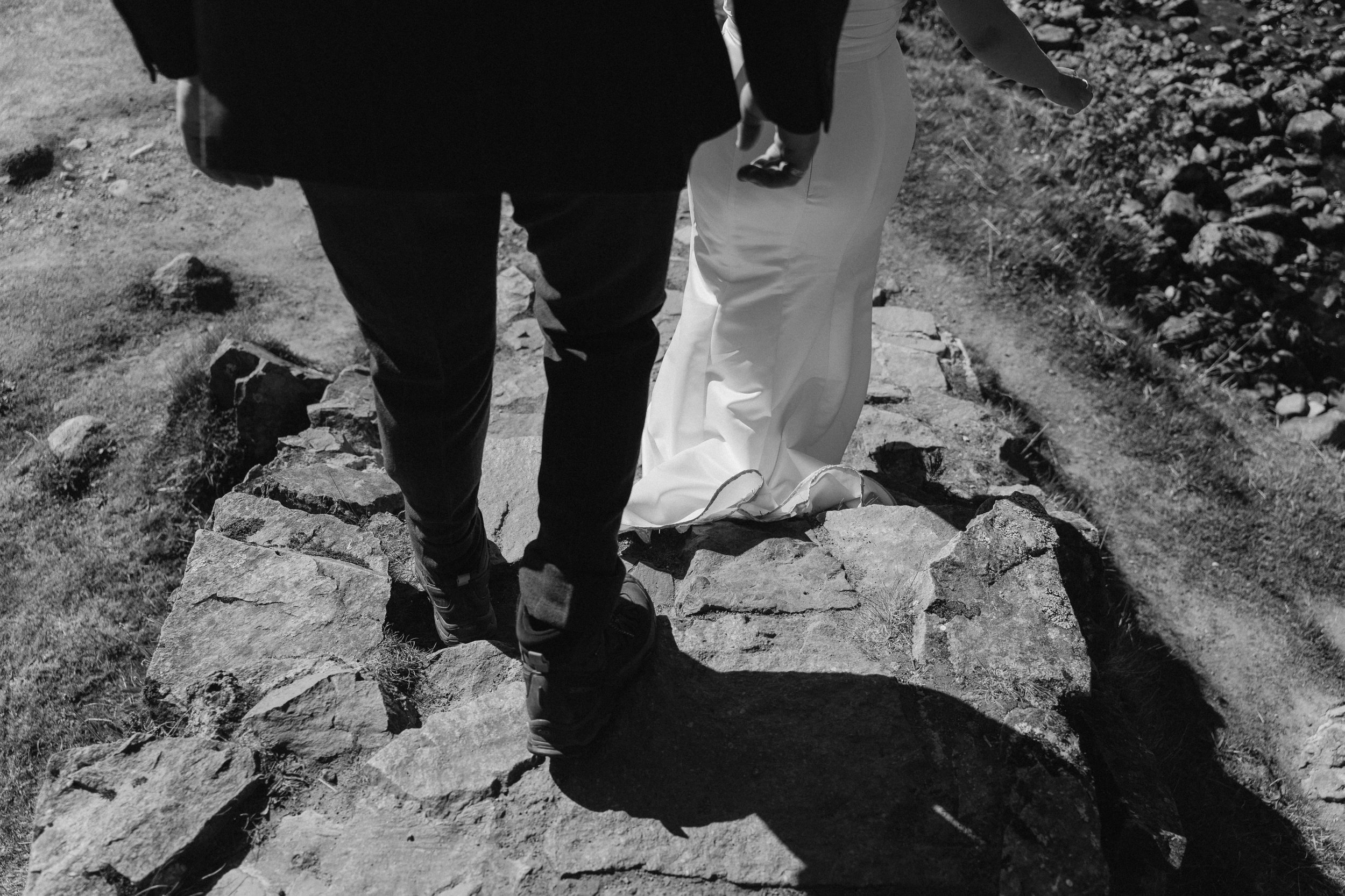 Close-up of a couple walking on a stone path, with only the lower half of their bodies visible; the woman is wearing white pants and the man is in dark pants and shoes. - captured by an Edinburgh wedding photographer