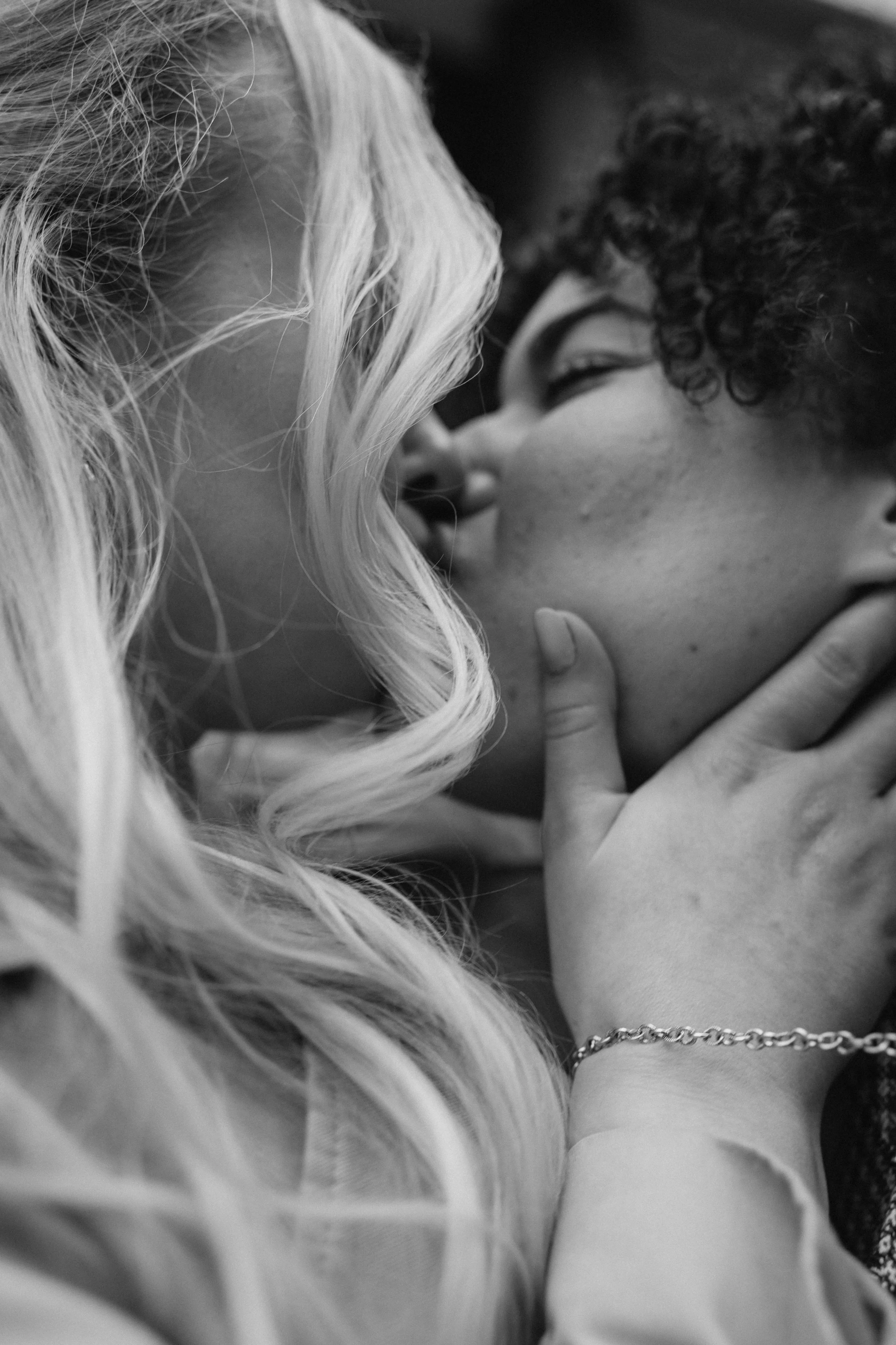 A close-up black-and-white photo of two women sharing a kiss, with one woman gently holding the other's face. - captured by an Edinburgh wedding photographer