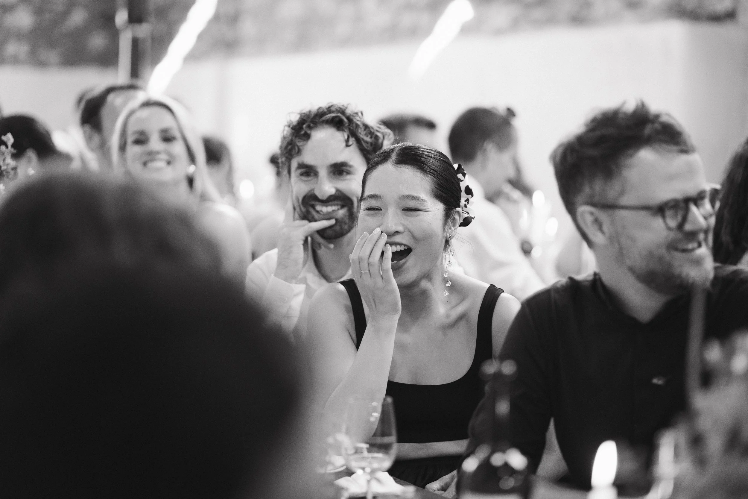 People laughing and enjoying themselves at a social gathering or party, seated at a table with glasses and drinks in front of them. - captured by an Edinburgh wedding photographer