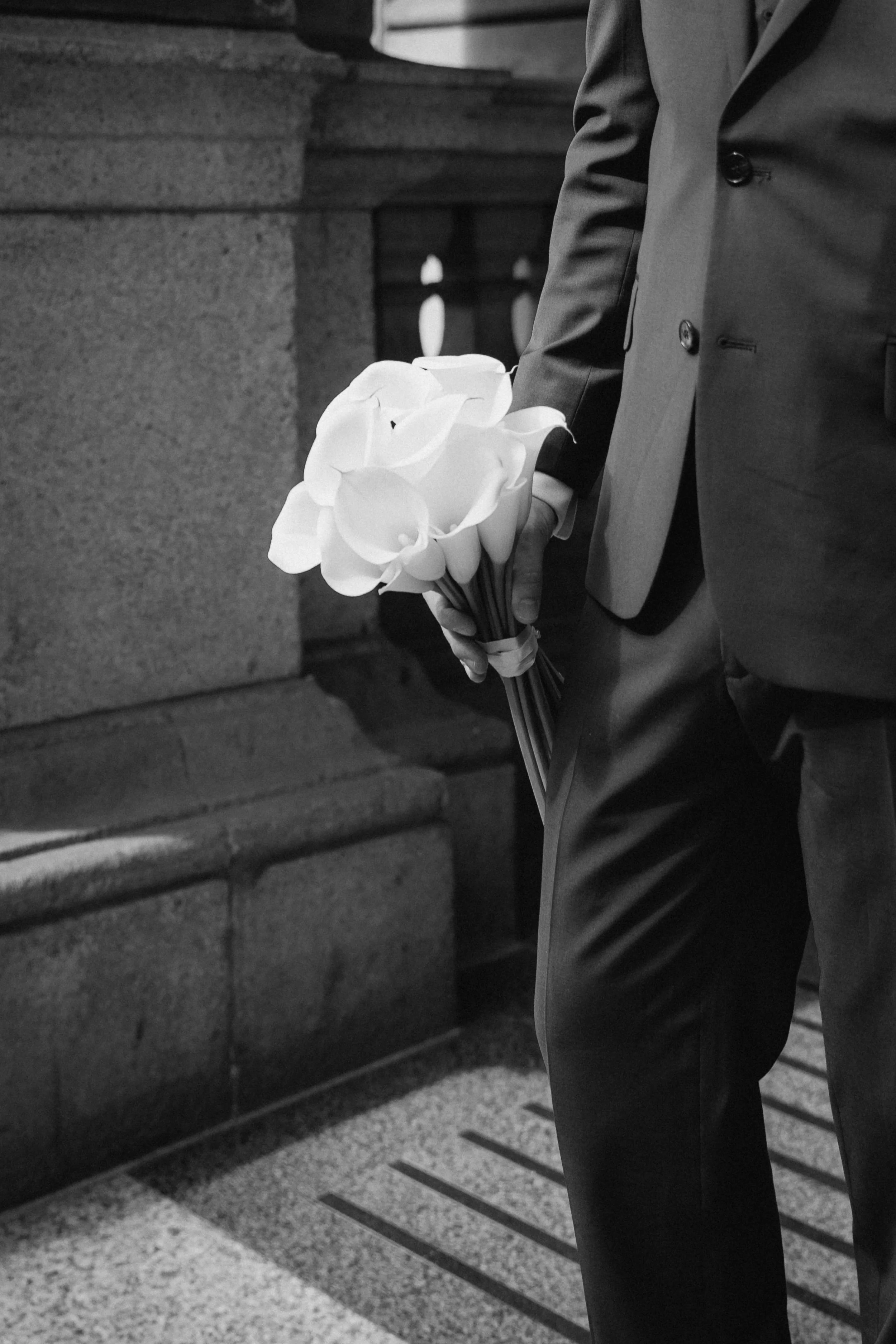 A man in a suit holding a bouquet of white calla lilies in his hand. - captured by an Edinburgh wedding photographer