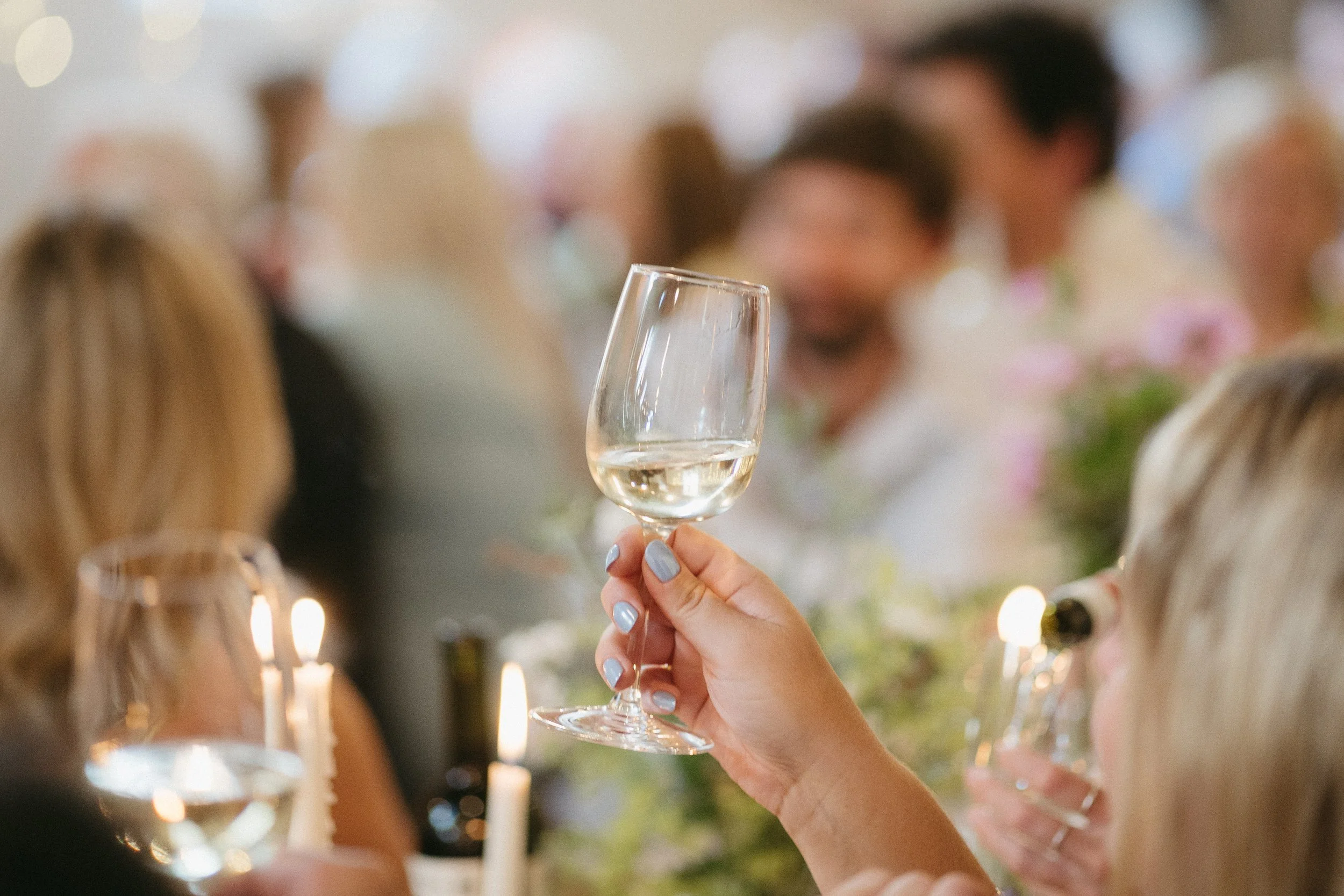 Person holding a glass of white wine at a celebration or social gathering with people in the background. - captured by an Edinburgh wedding photographer