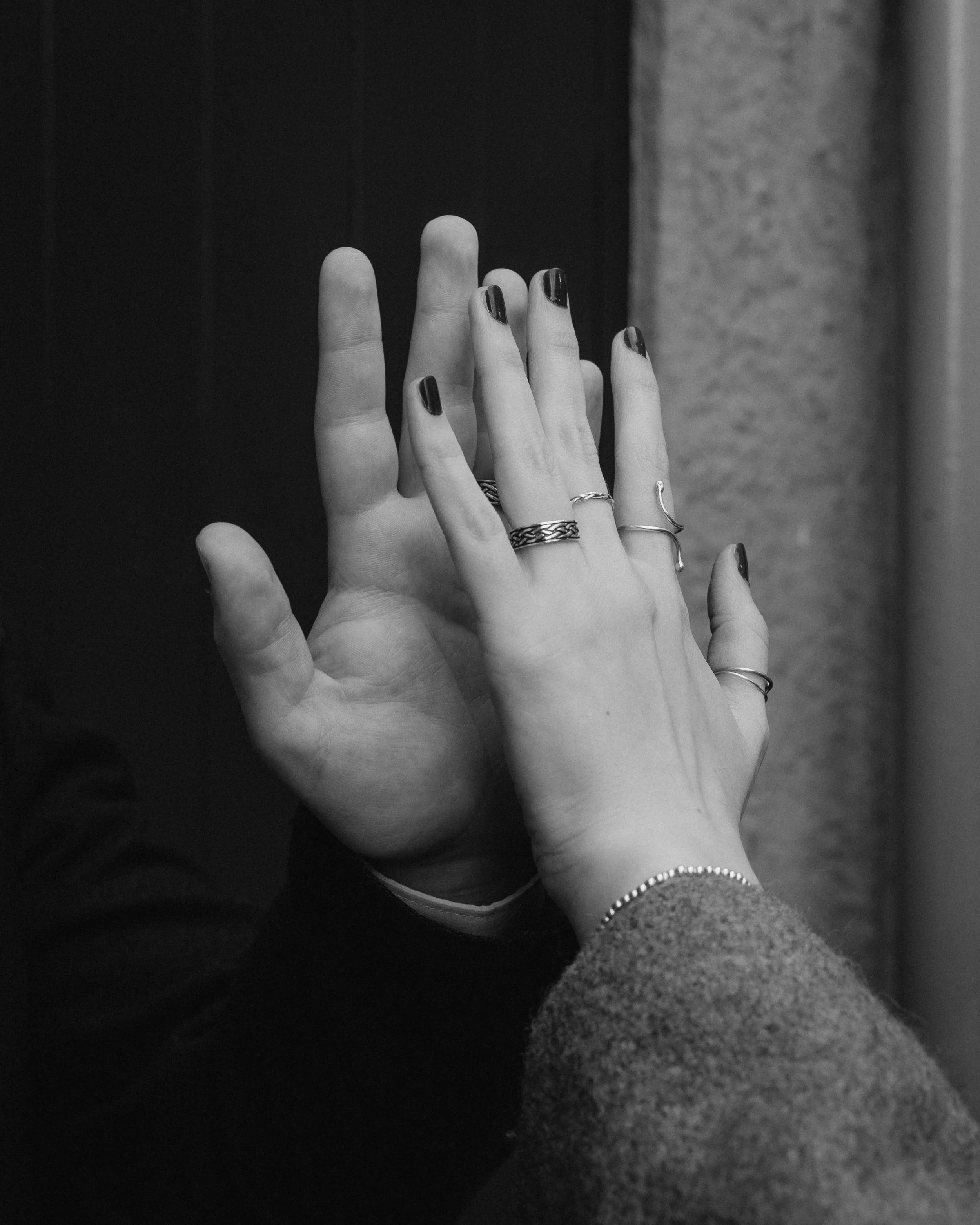 Two hands reaching out to each other, with one hand wearing rings and the other with a bracelet, against a textured background in black and white. - captured by an Edinburgh wedding photographer